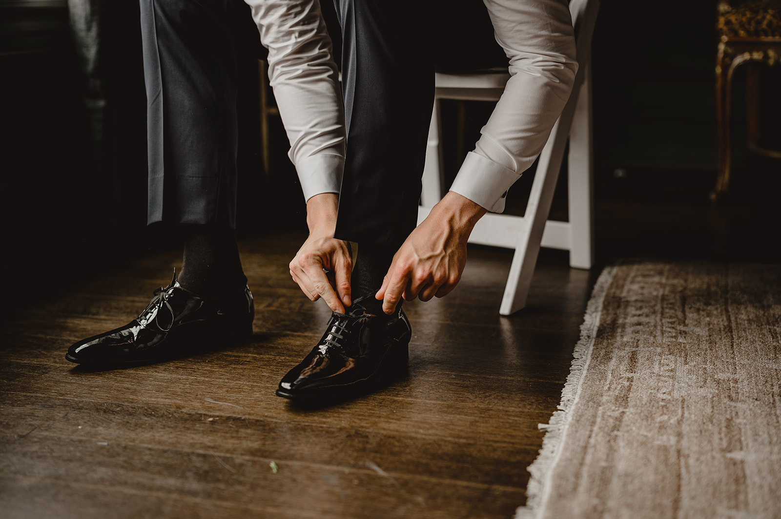groom laces up shiny black shoes against hardwood floor