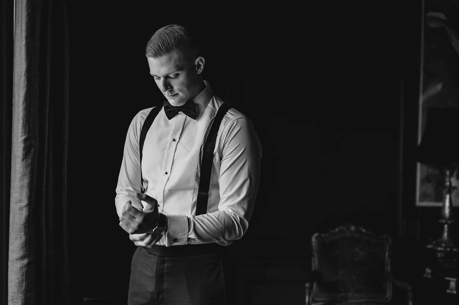 black and white portrait of groom adjust cufflinks in room