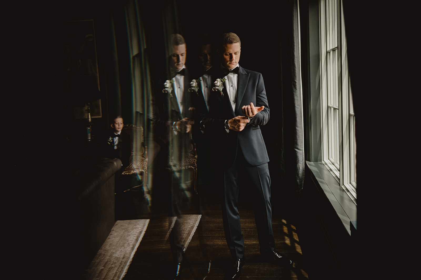 groom leans against mirror in suite prepping his watch and cufflinks