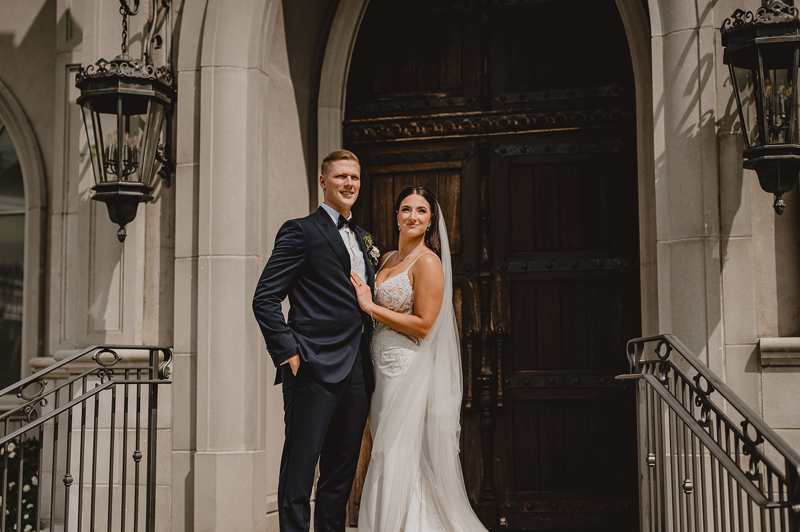 bride and groom stand on top of steps in front of wooden door at Park Chateau chapel