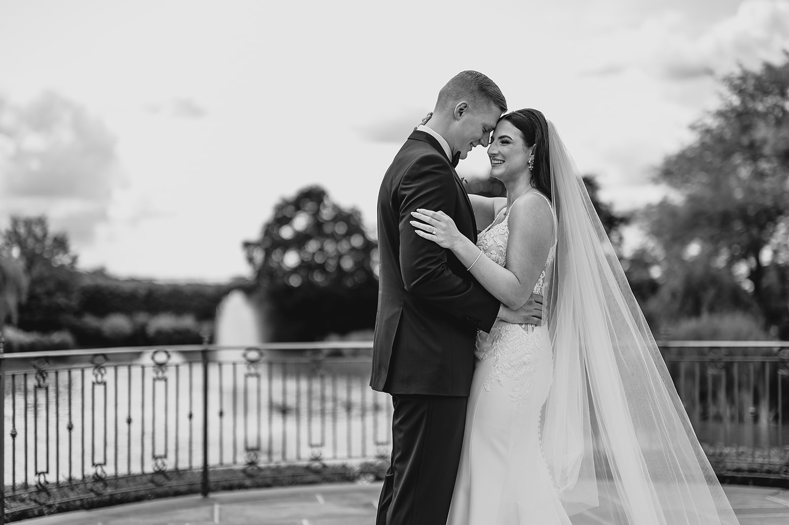 bride and groom lean heads together on patio by fountain