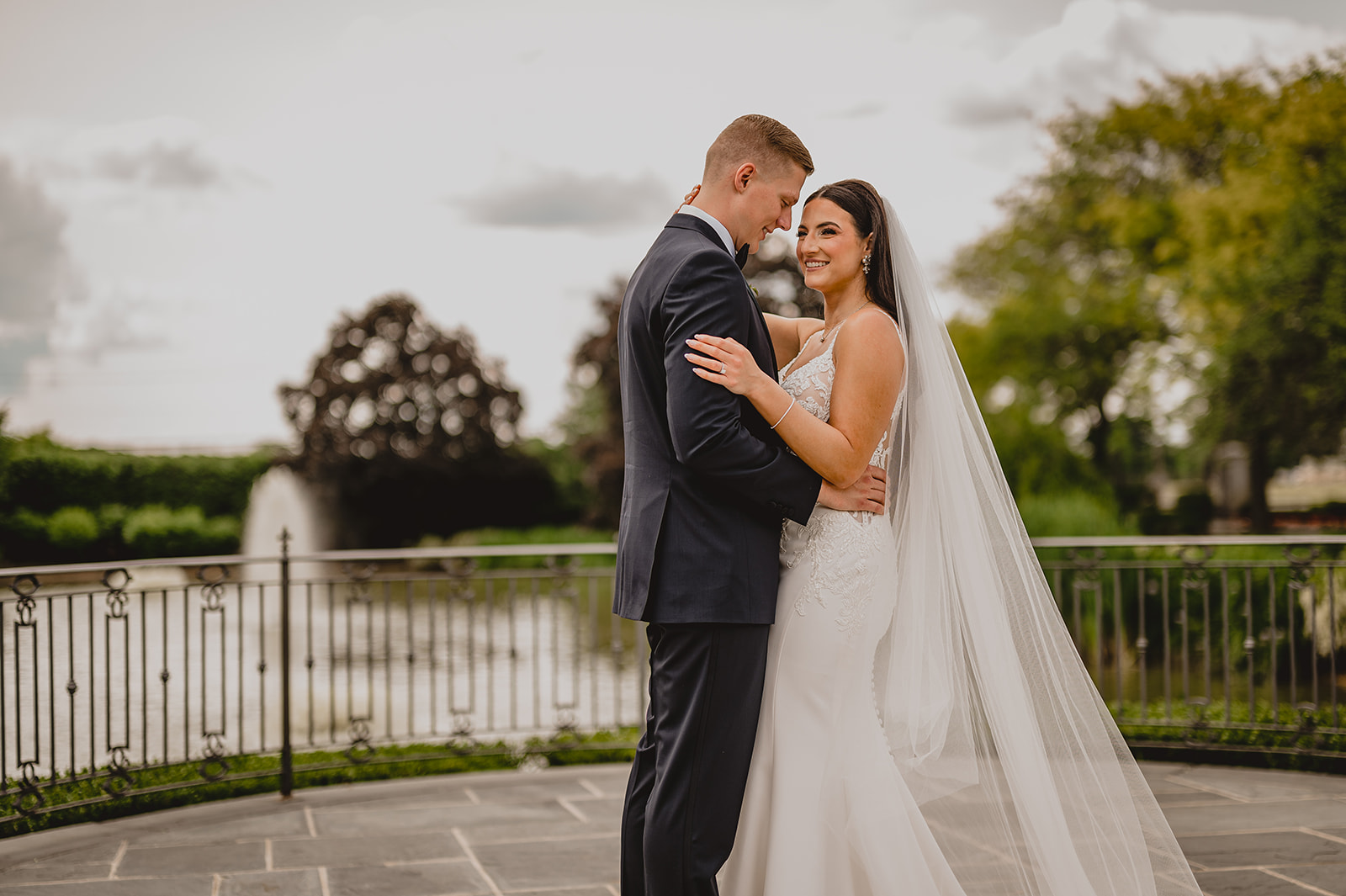 newlyweds hug on patio by fountain at Park Chateau Estate