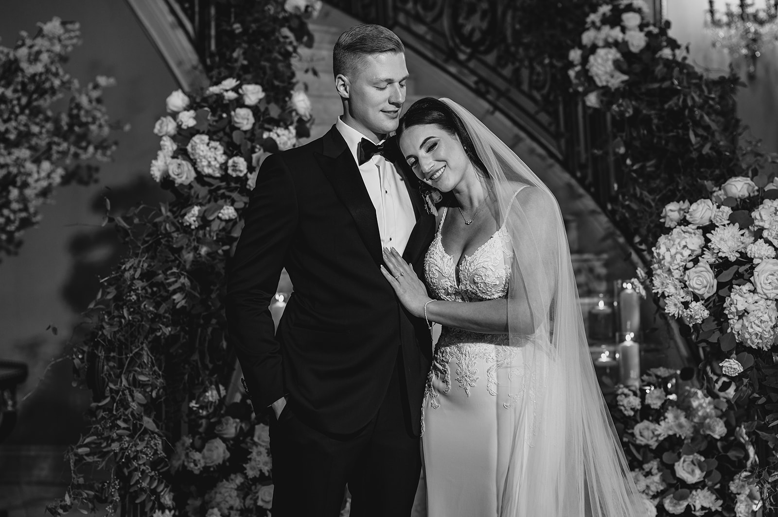 bride leans head on groom's chest at bottom of flower covered staircase inside Park Chateau Estate