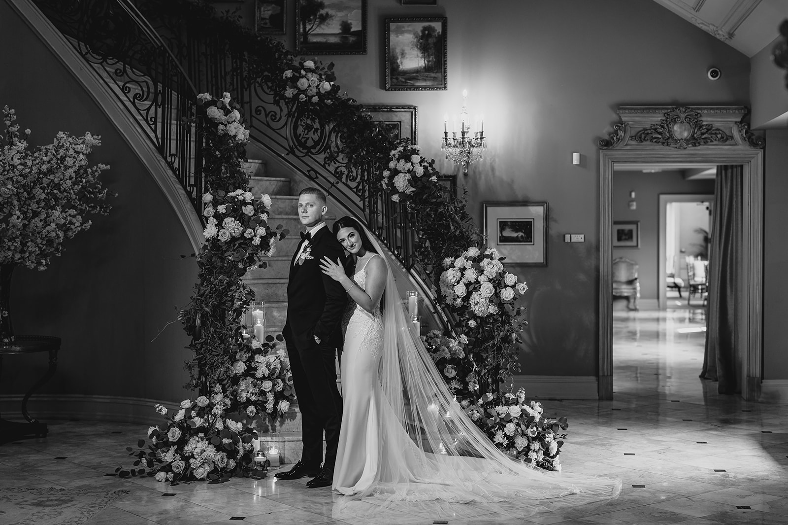 bride hugs groom from behind at bottom of flower covered staircase inside Park Chateau Estate