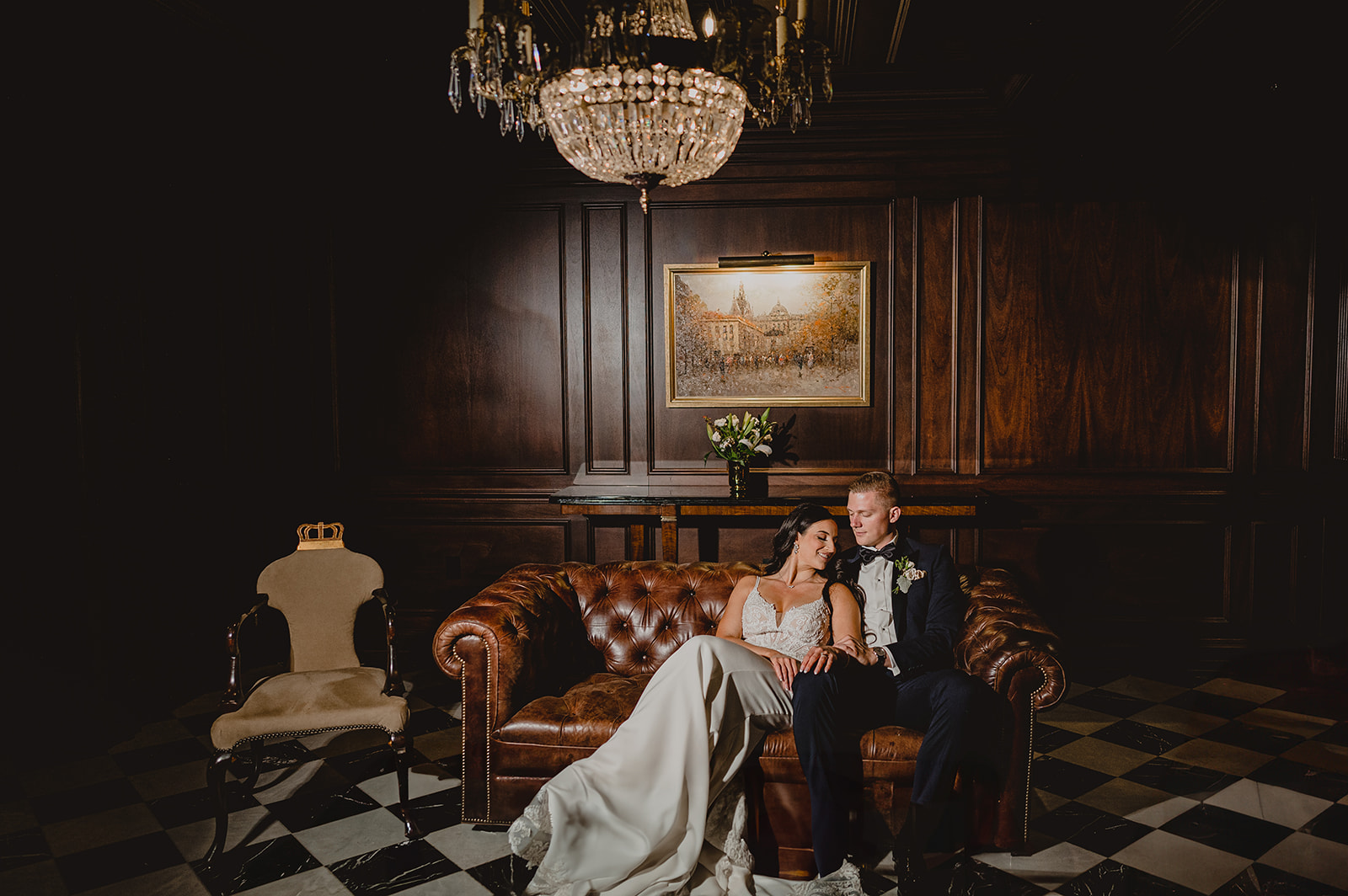 newlyweds sit on leather couch inside library at Park Chateau Estate