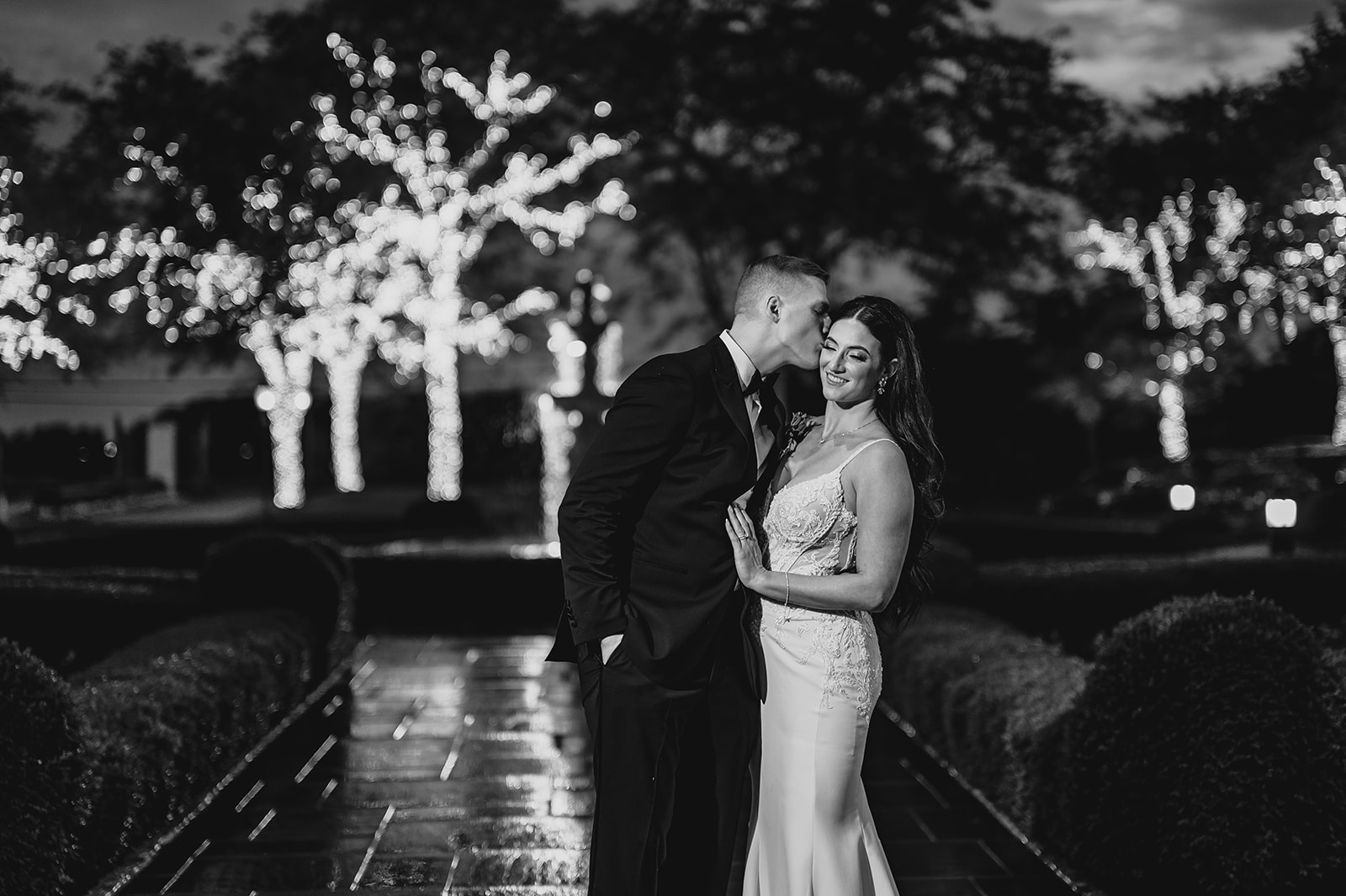 bride and groom hug outside at night with trees lit up
