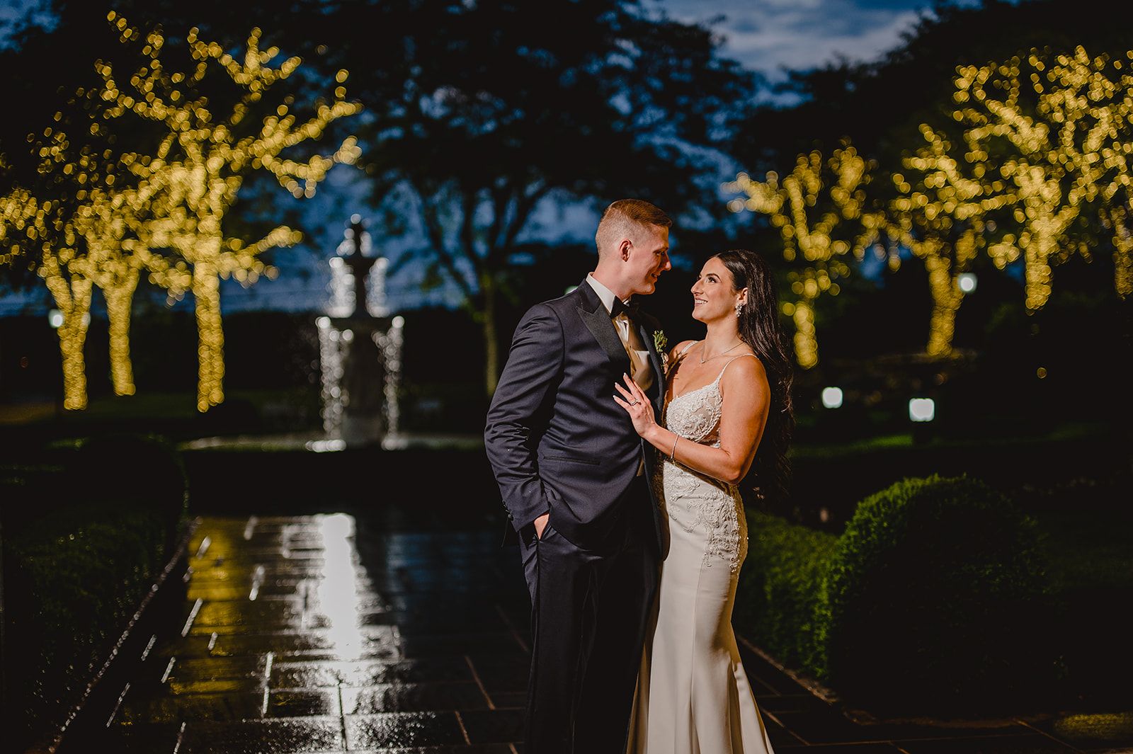 bride and groom hug outside at night with trees lit up
