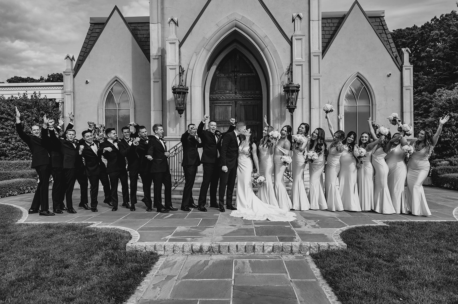 bride and groom kiss surrounded by bridal party outside leaving the Park Chateau Estate chapel