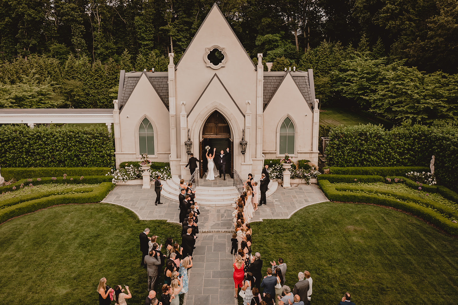 newlyweds leave Park Chateau Estate chapel with wedding guests down pathway