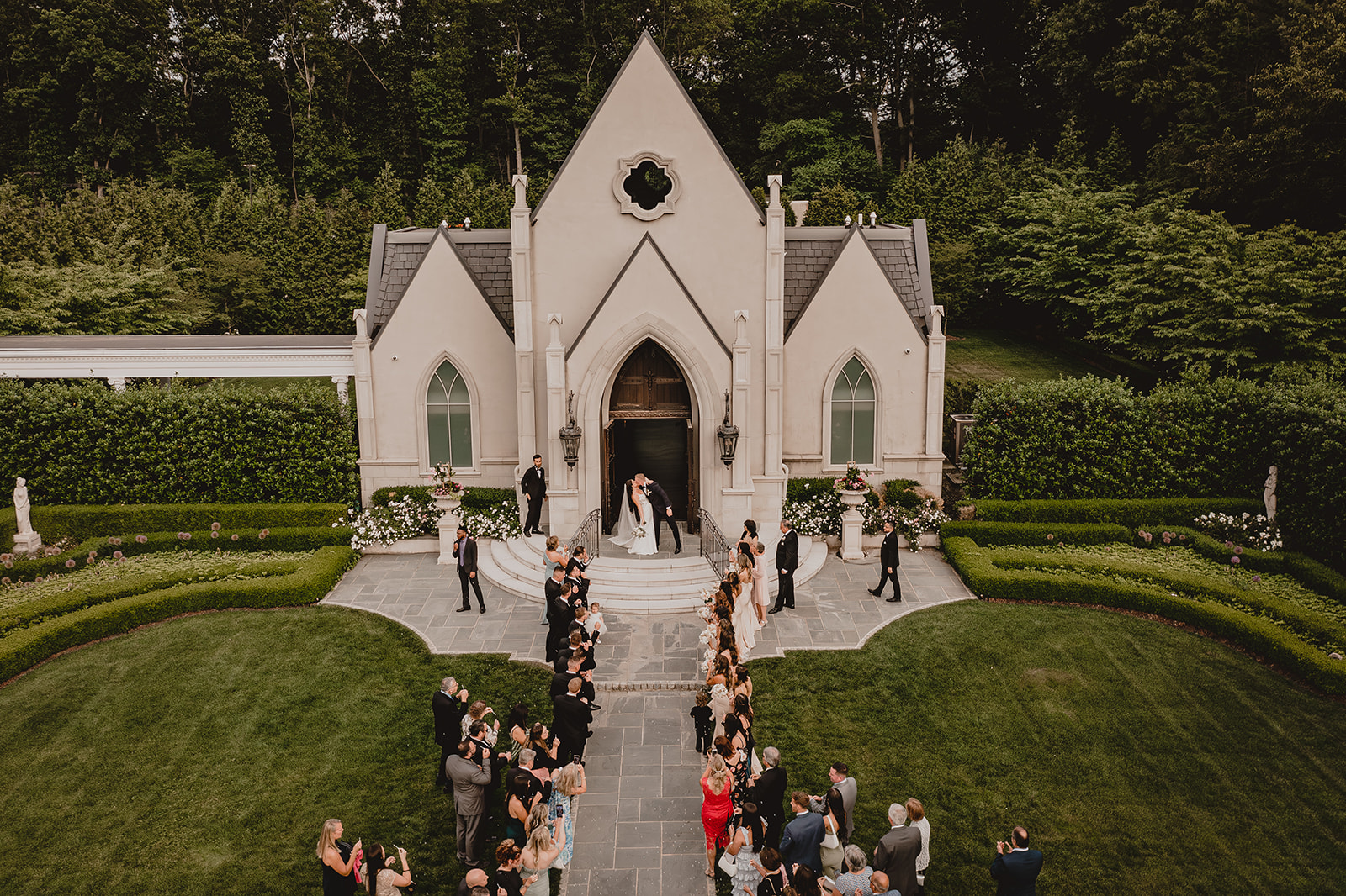 newlyweds leave Park Chateau Estate chapel with wedding guests down pathway