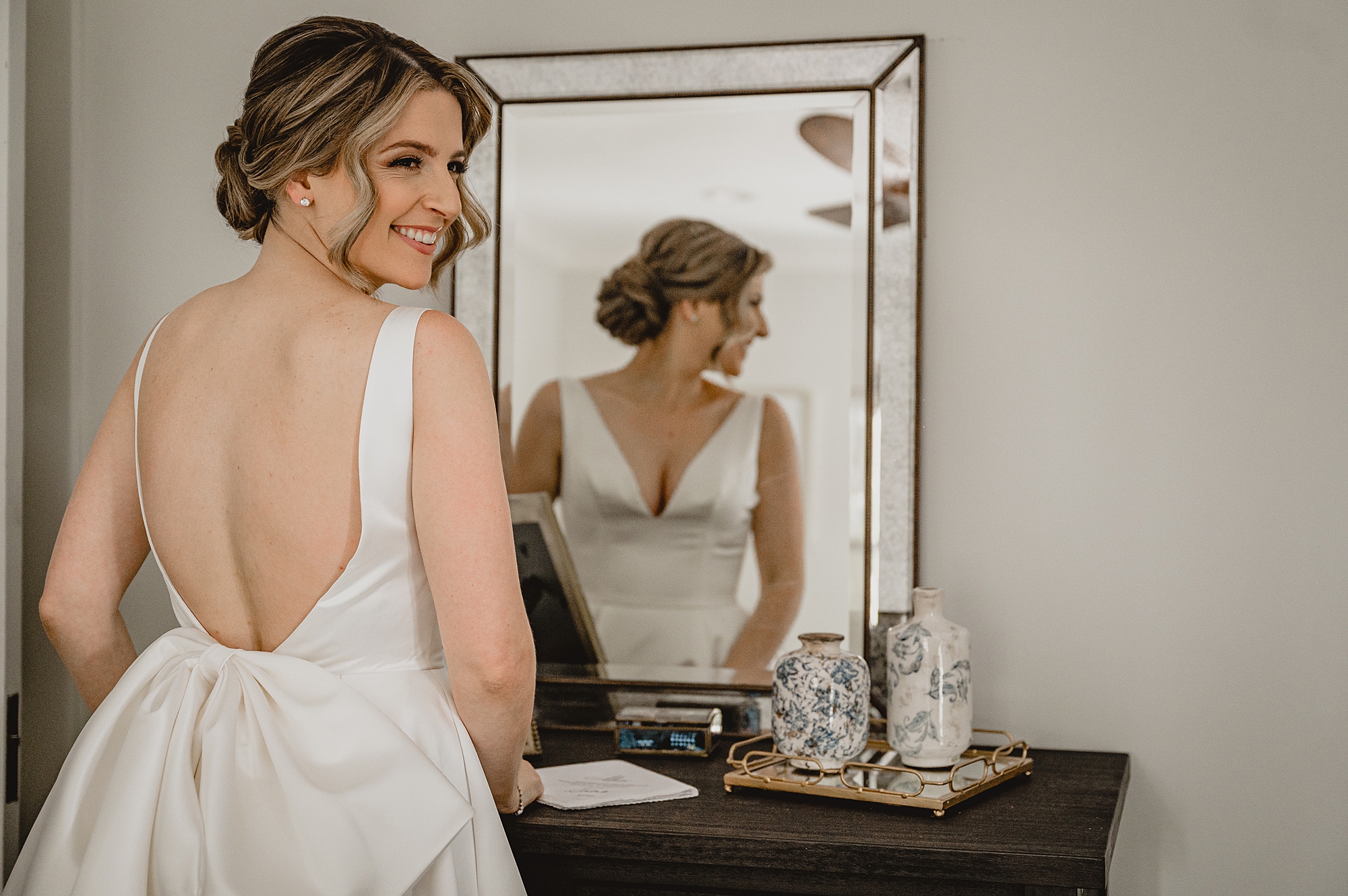 bride smiles over shoulder in front of mirror