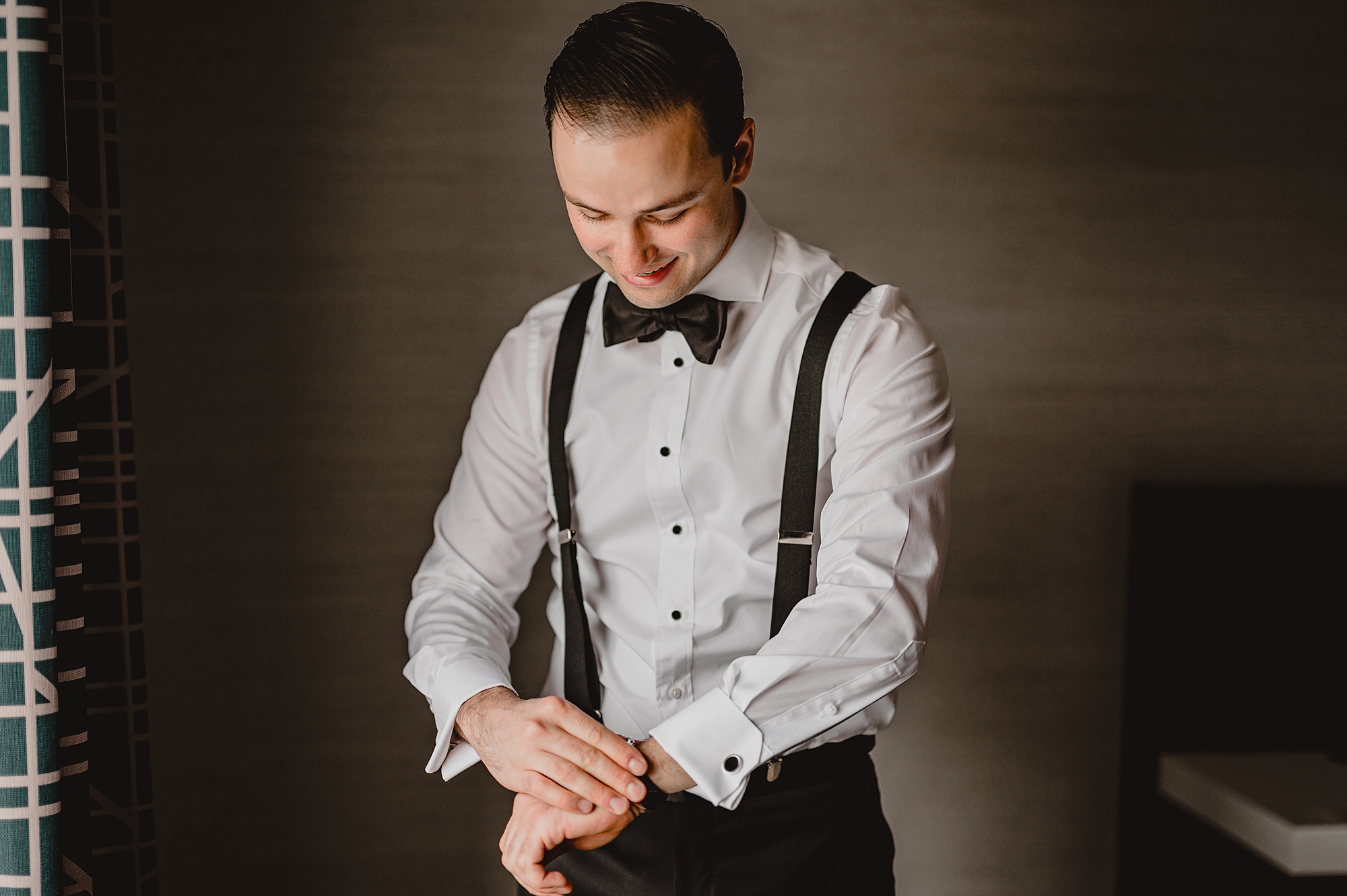 groom stands in suspenders adjusting cufflinks 