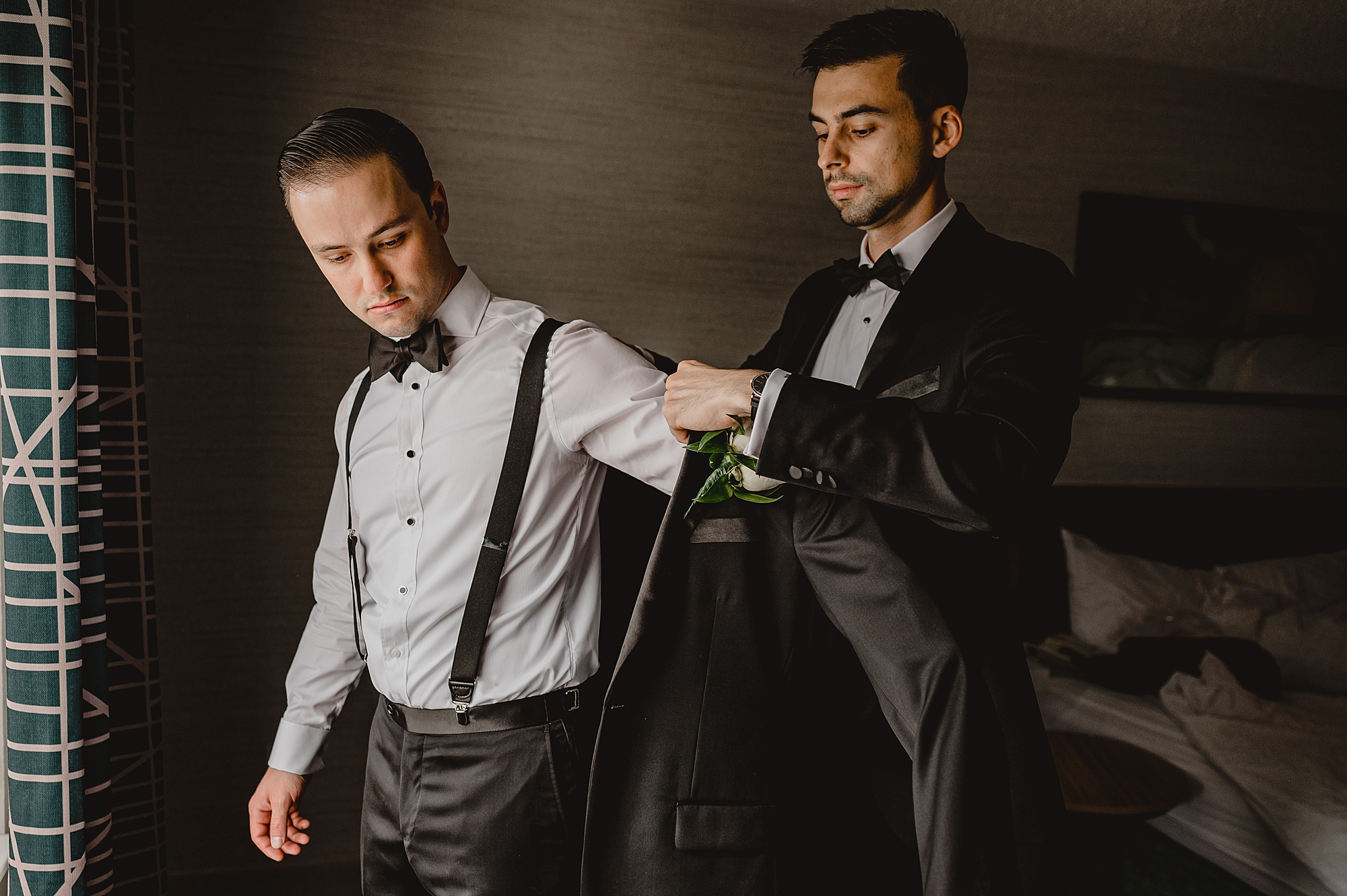 groomsman helps groom into stuff jacket 