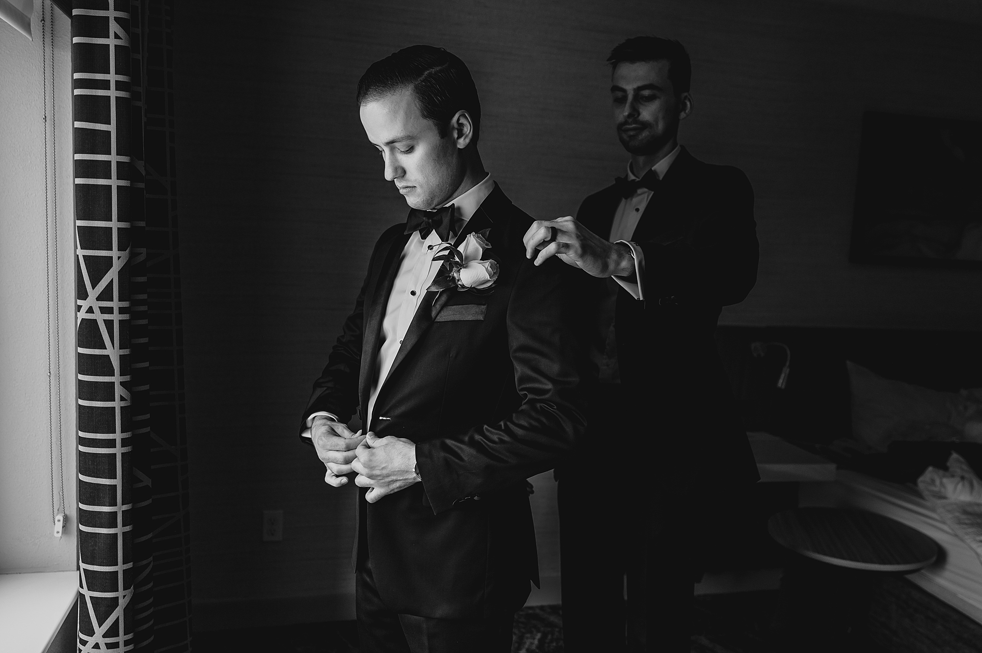 groomsman helps groom adjust jacket while preparing for Long Island wedding day 