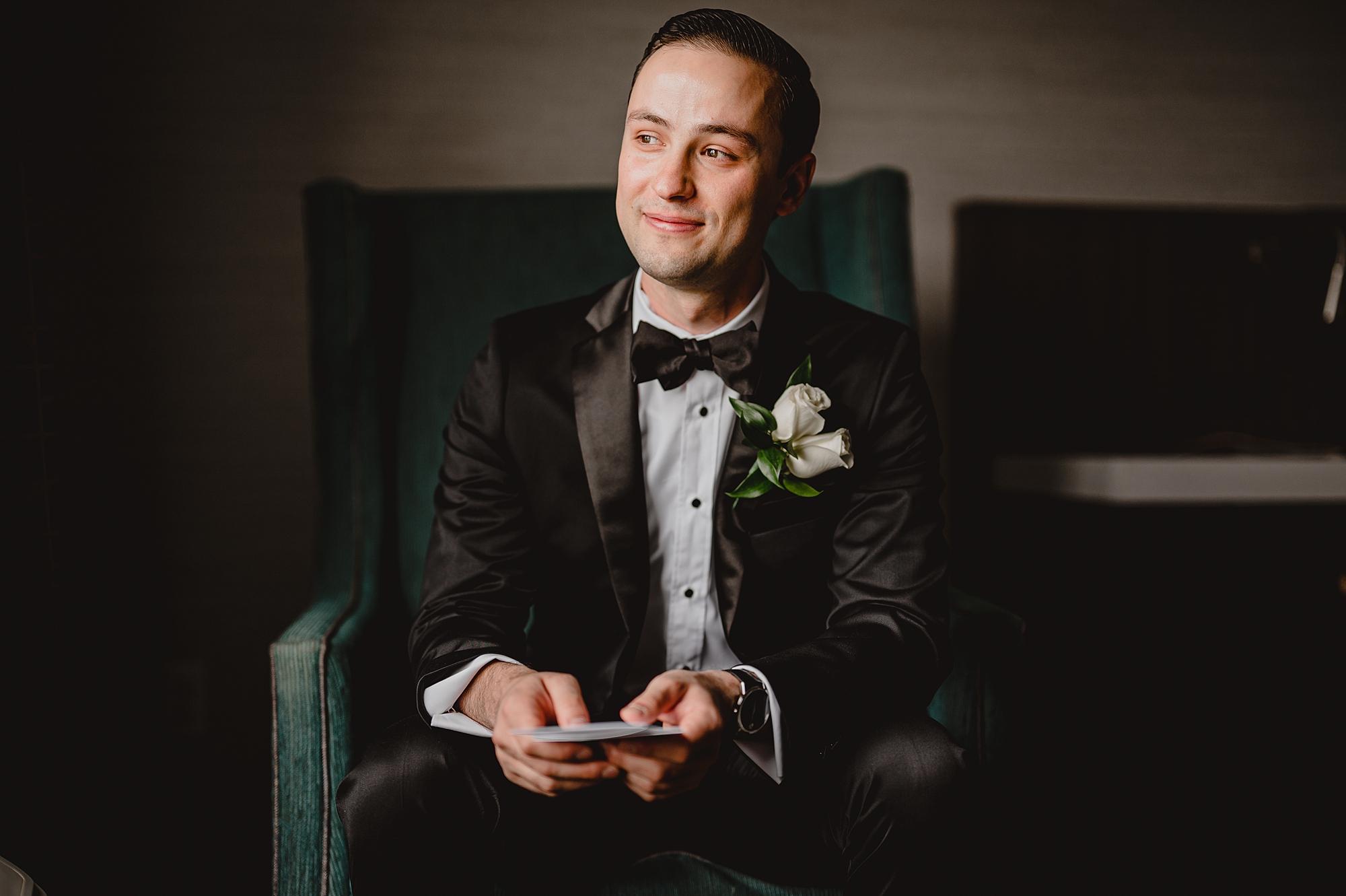 groom holds vow booklet sitting in suit 