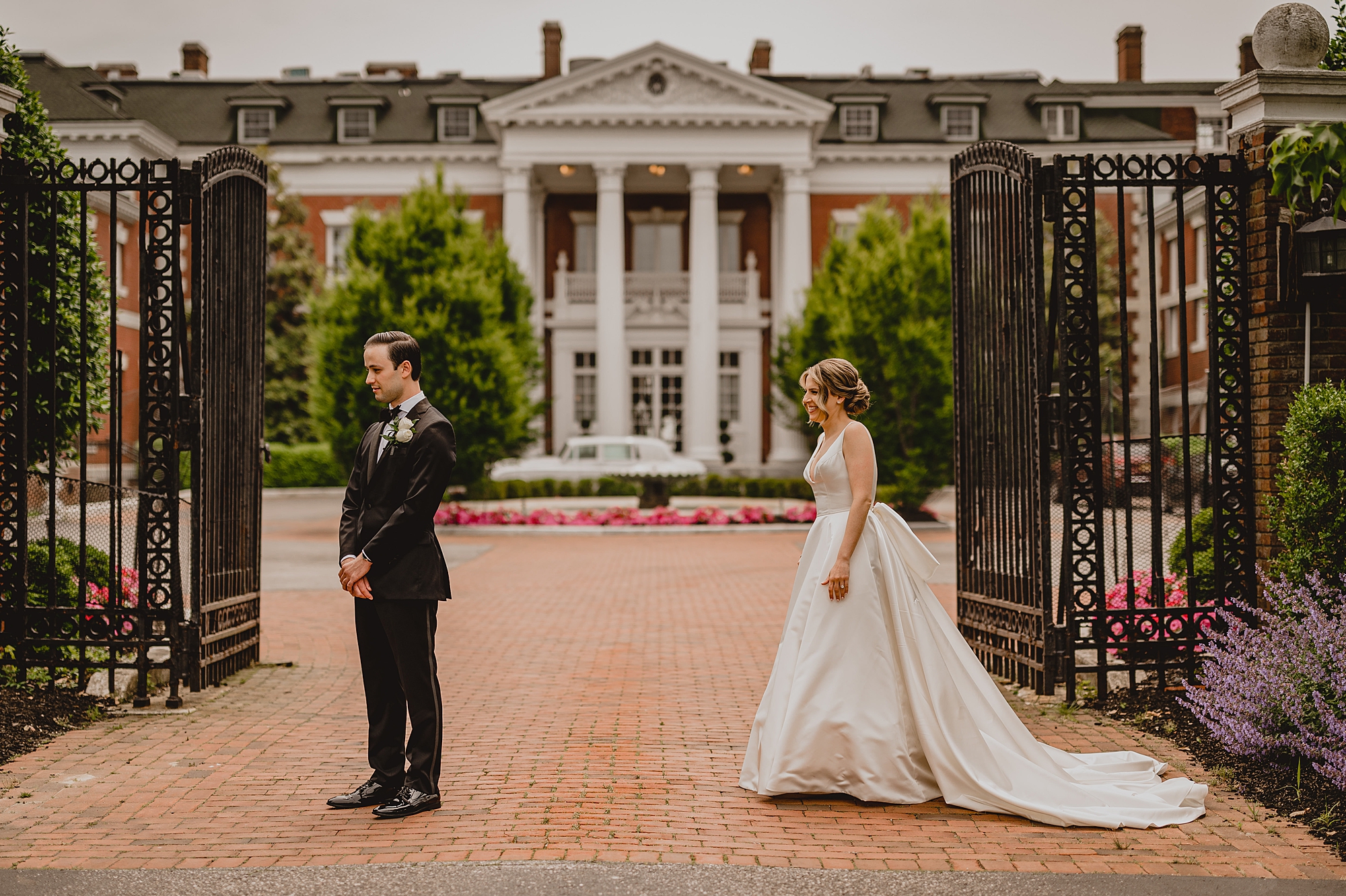 bride approaches groom for first look by iron gates at Bourne Mansion