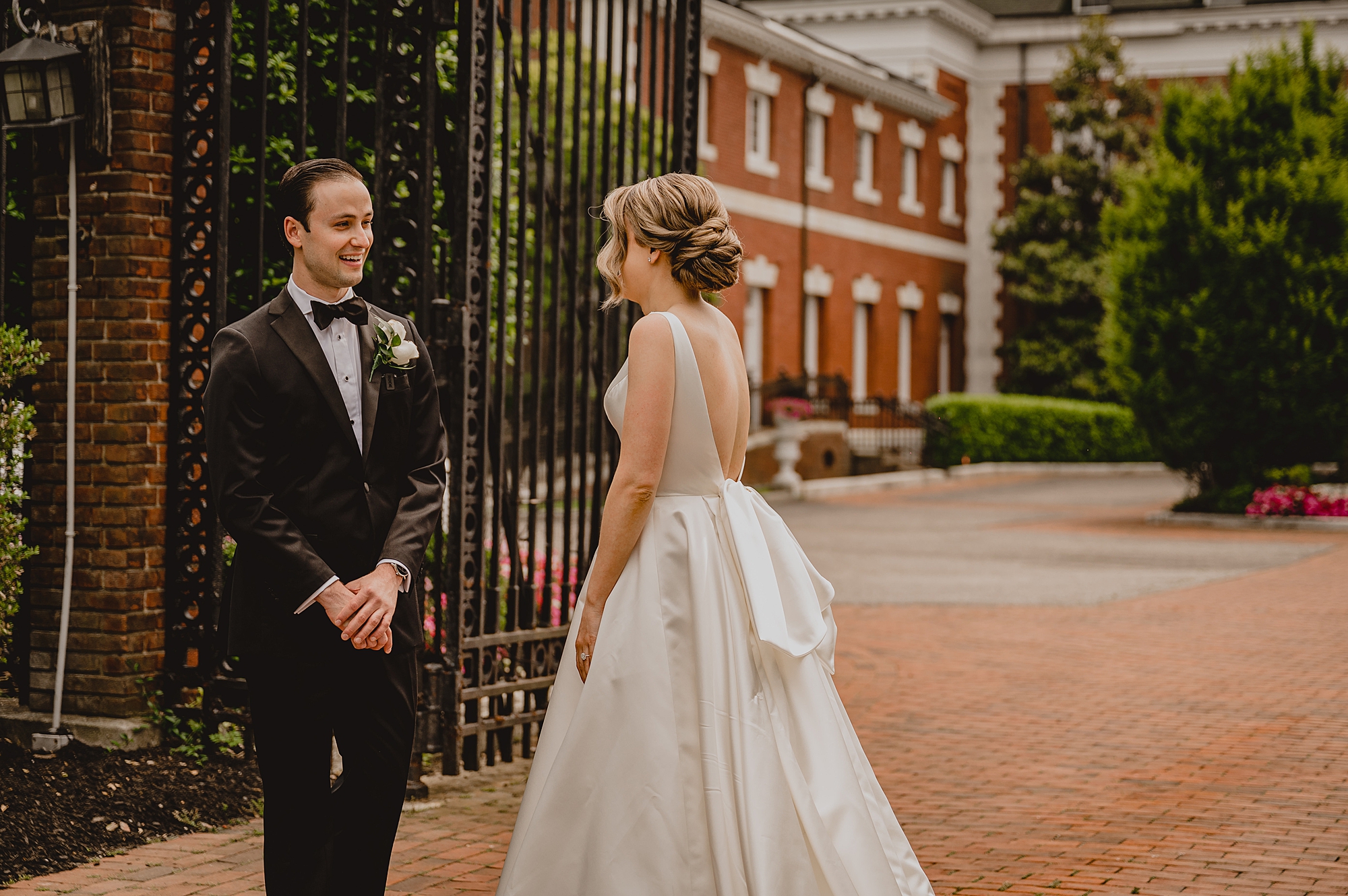 bride approaches groom during first look outside iron gates at Bourne Mansion