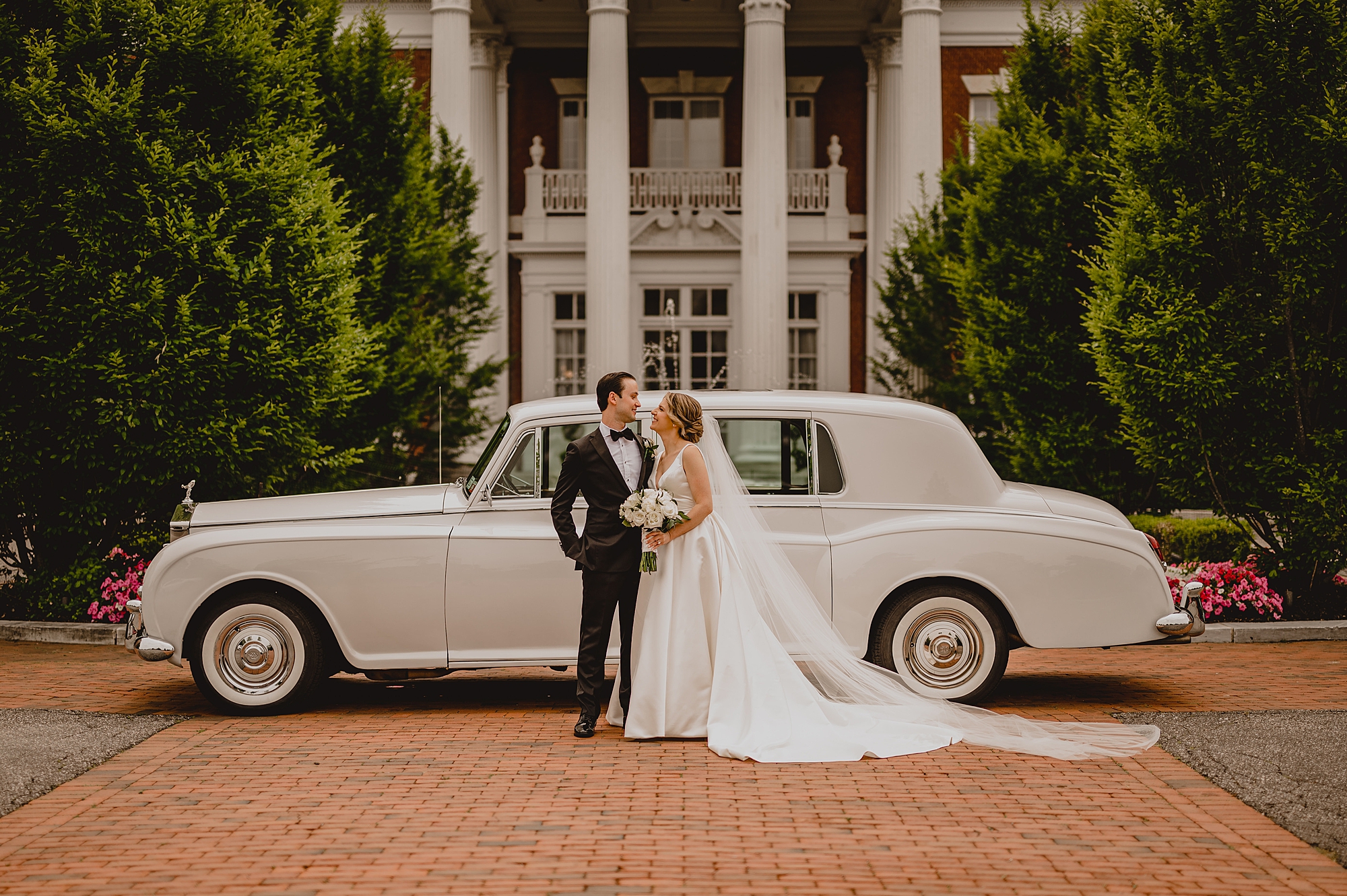 bride and groom hug by vintage white car at Bourne Mansion
