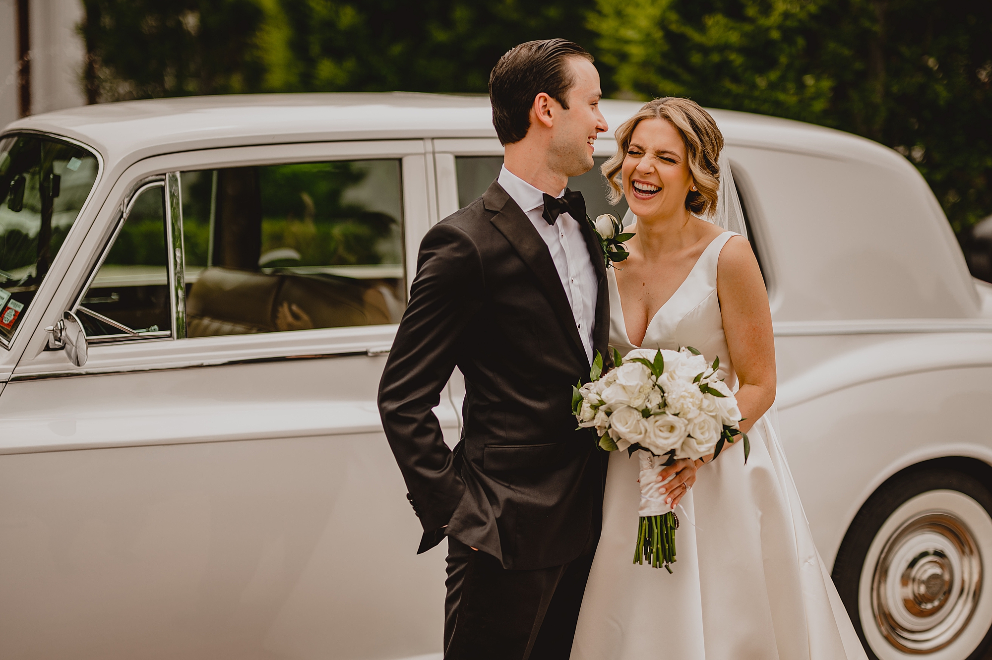 bride and groom hug by vintage white car at Bourne Mansion