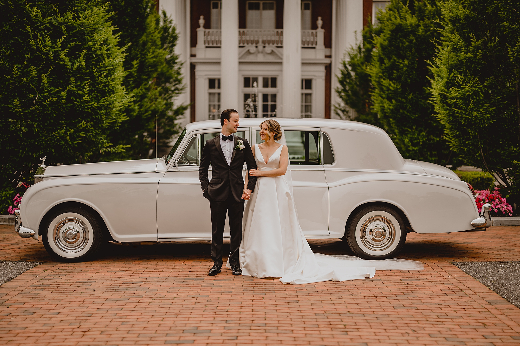 bride and groom hug by vintage white car at Bourne Mansion