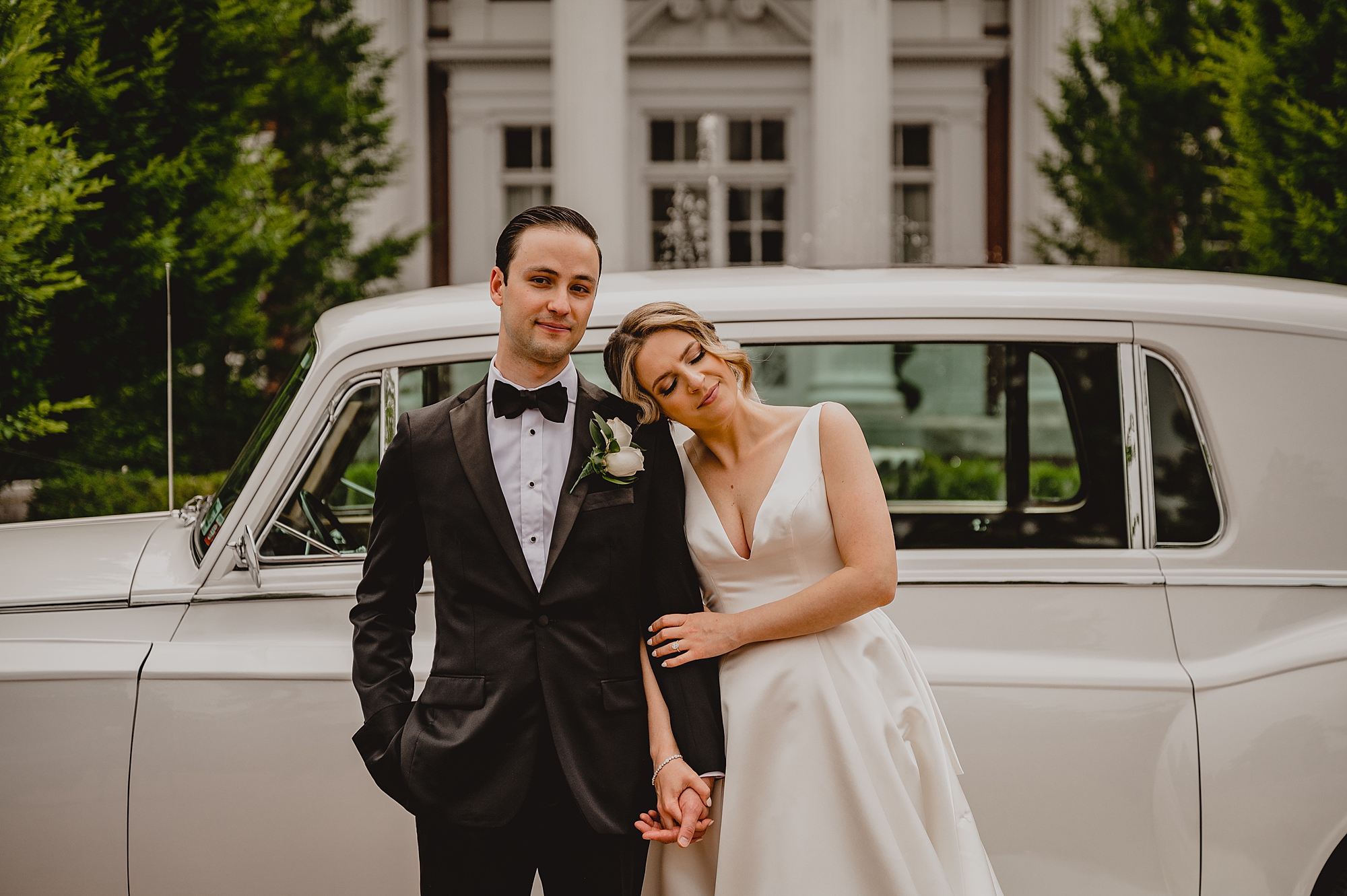 bride and groom hug by vintage white car at Bourne Mansion