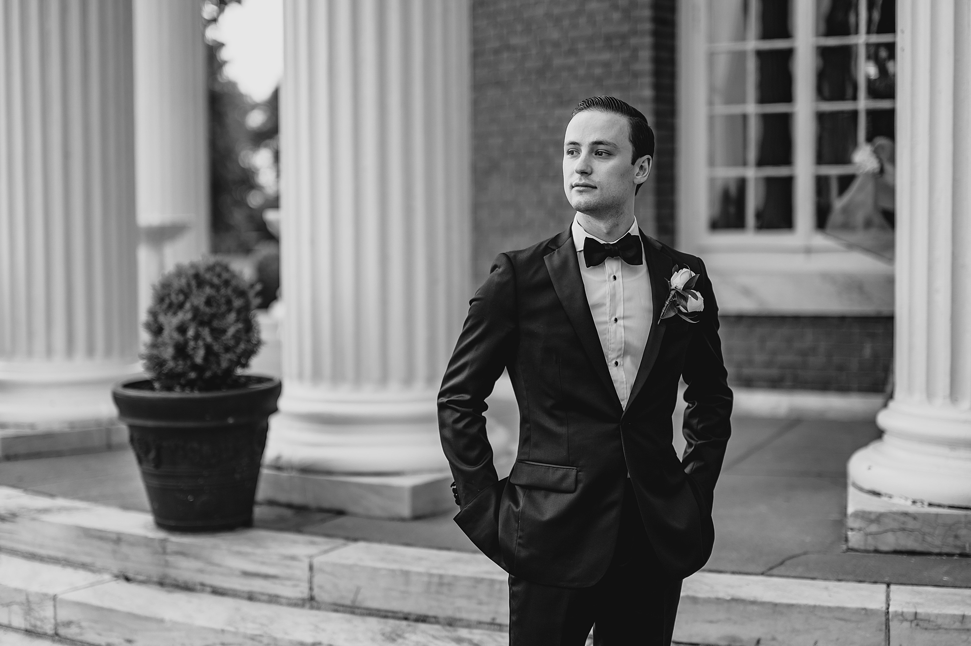 groom stands with hands in pockets outside Bourne Mansion