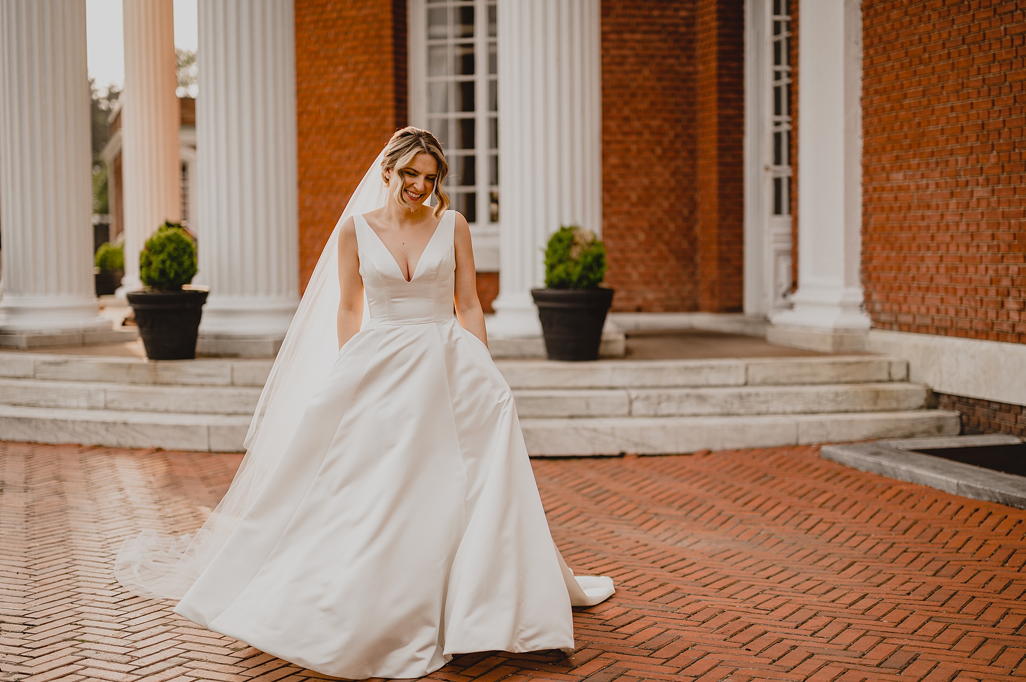 bride holds skirt of wedding dress walking outside Bourne Mansion