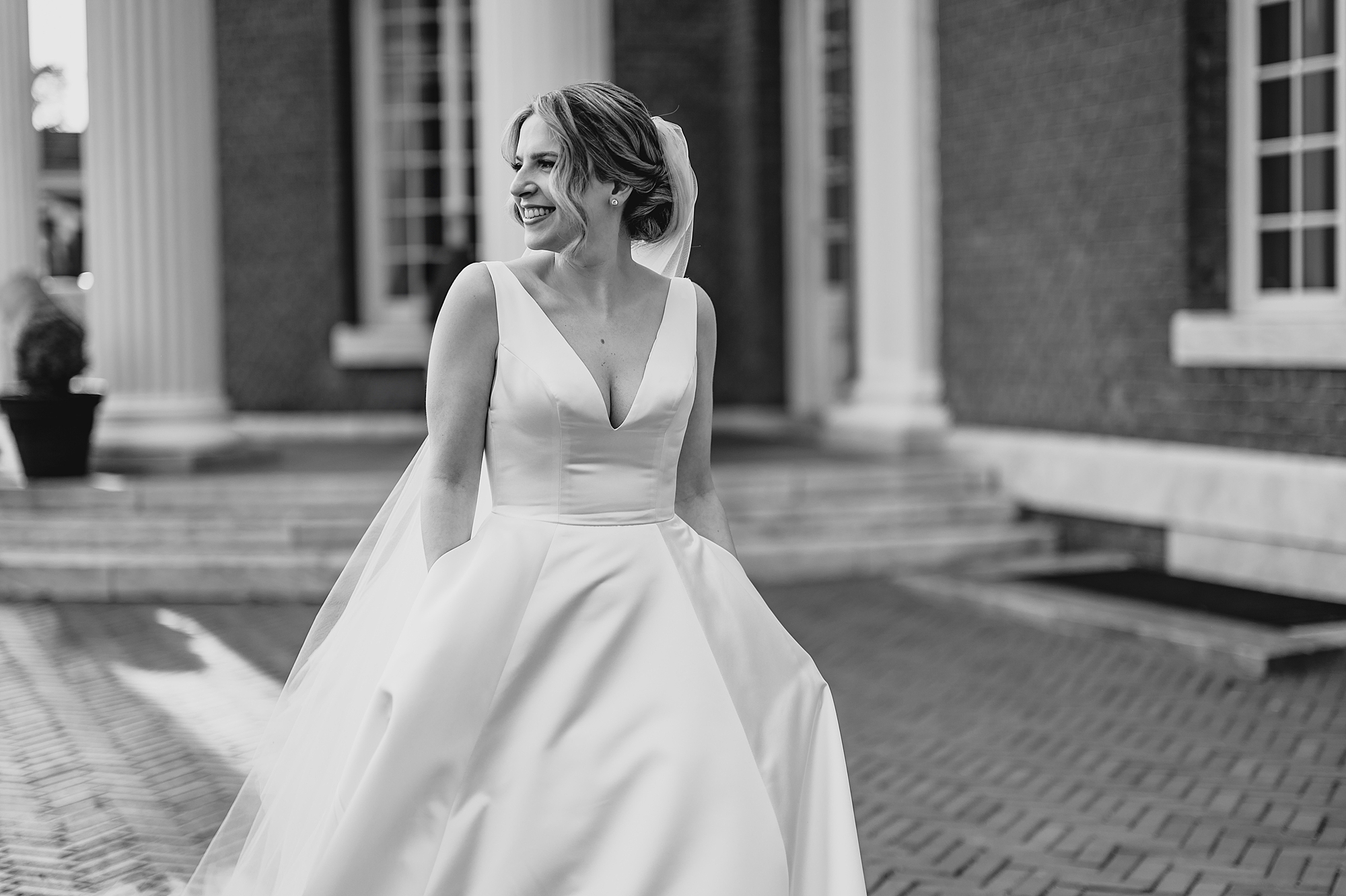 bride walks outside Bourne Mansion with hands in pocket of wedding dress