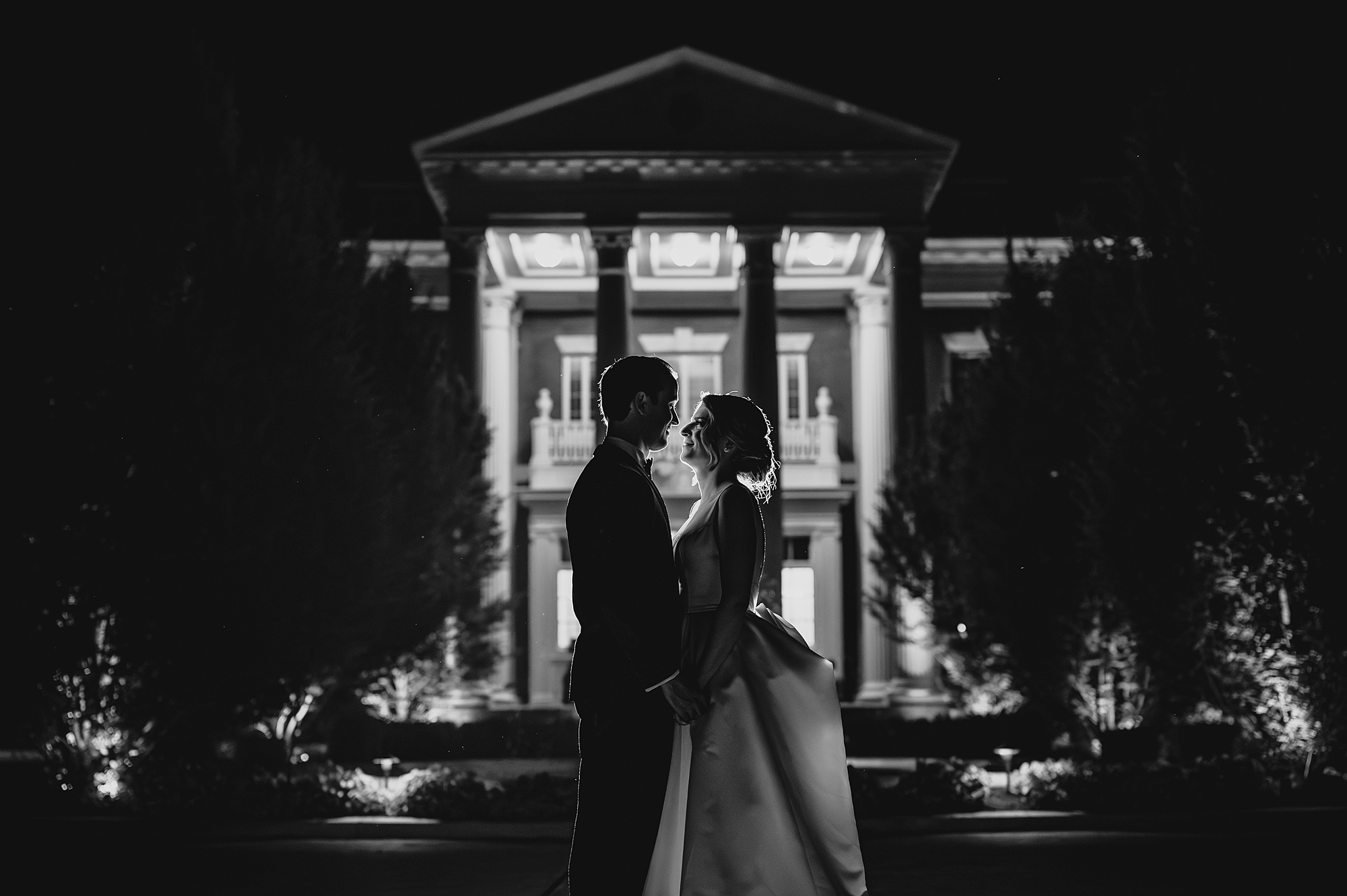 newlyweds hold hands outside Bourne Mansion at nighttime