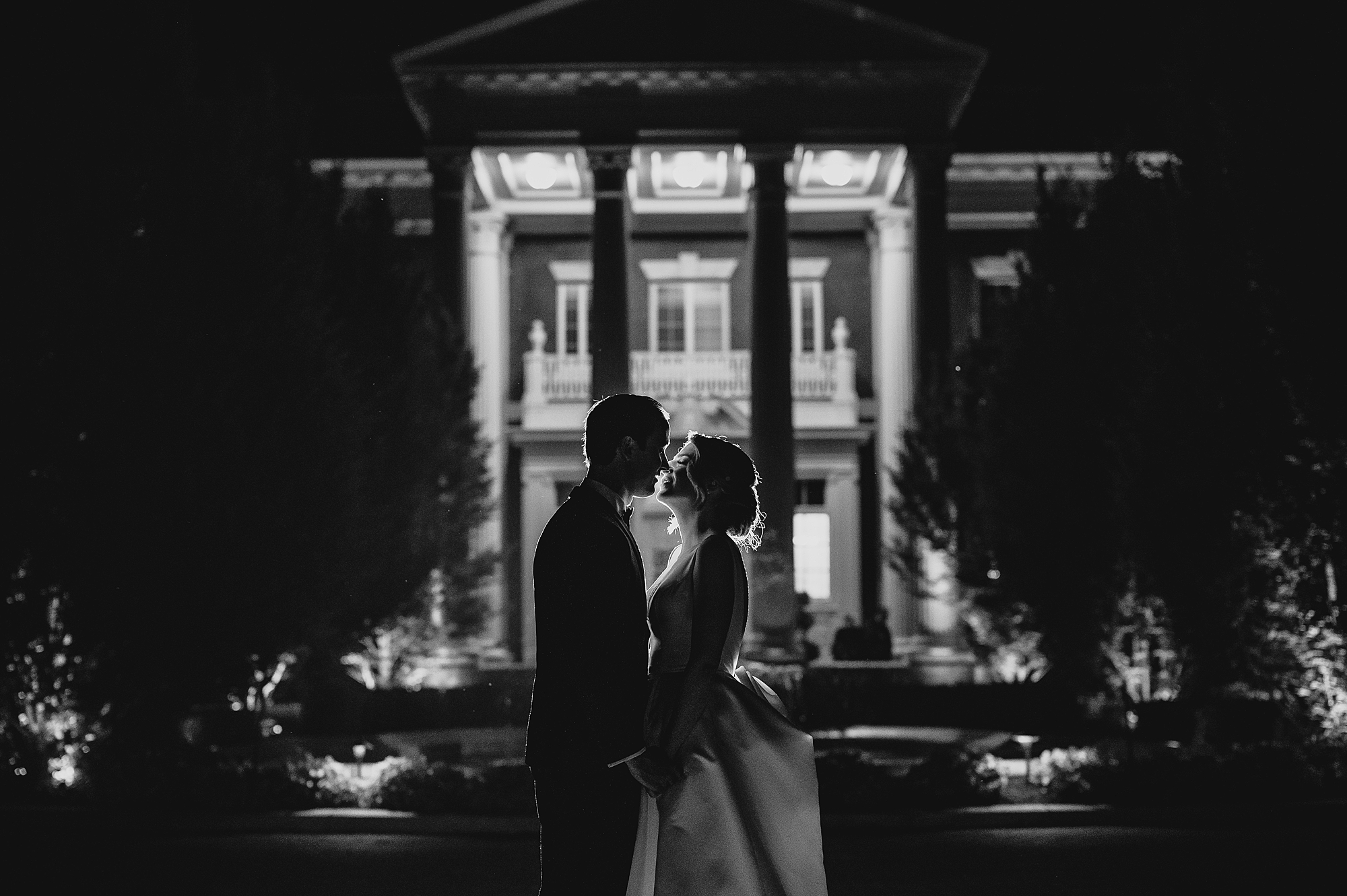 newlyweds hold hands outside Bourne Mansion at nighttime