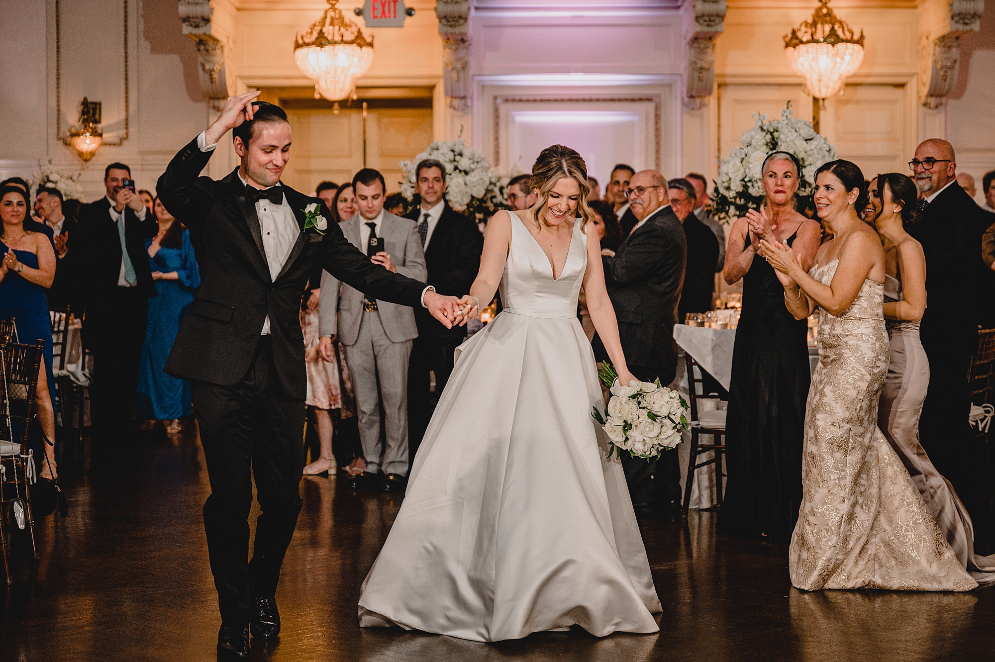 newlyweds hold hands walking onto dance floor at Bourne Mansion