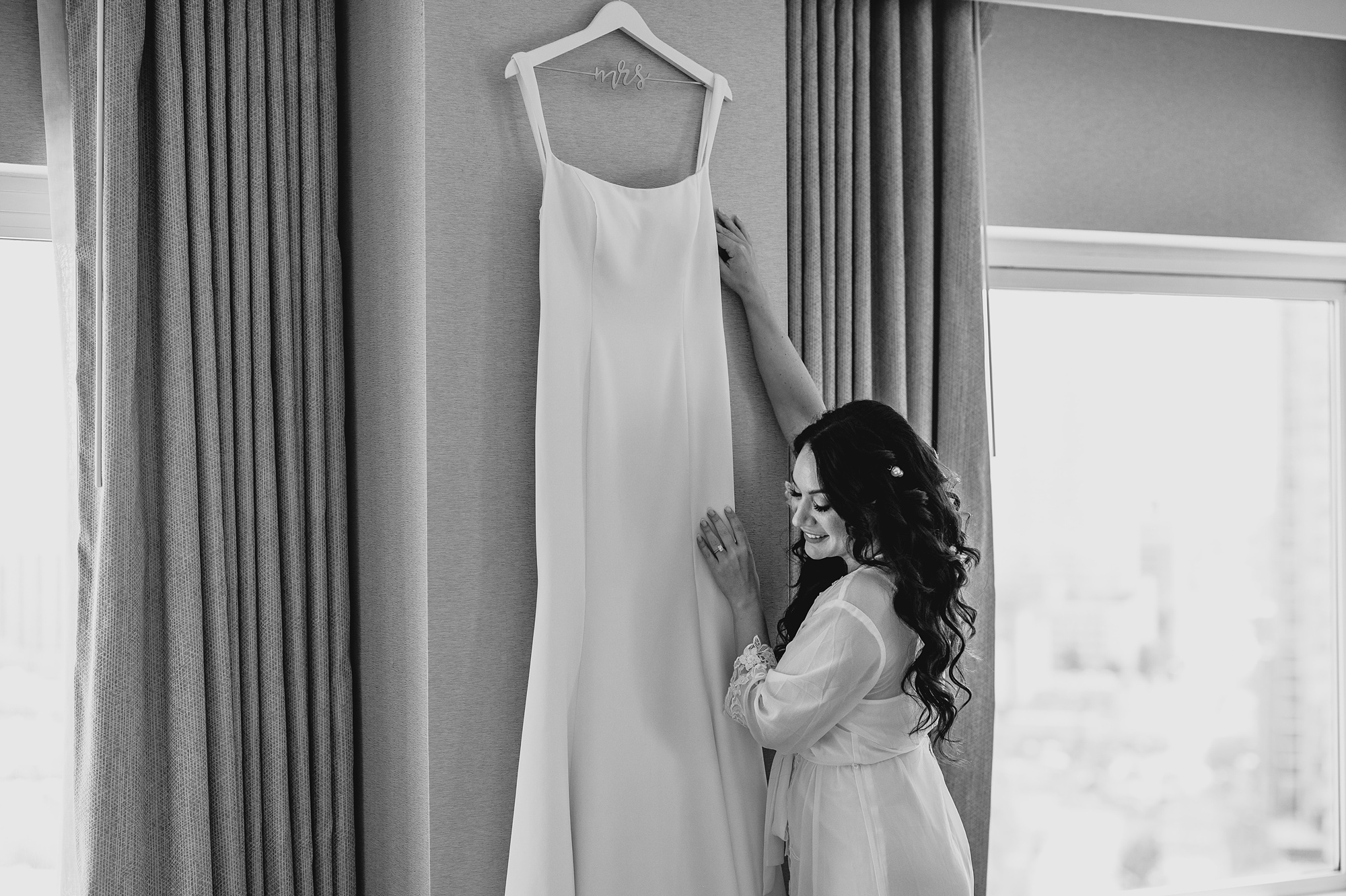 bride reaches for wedding dress hanging on wall of hotel in New Jersey