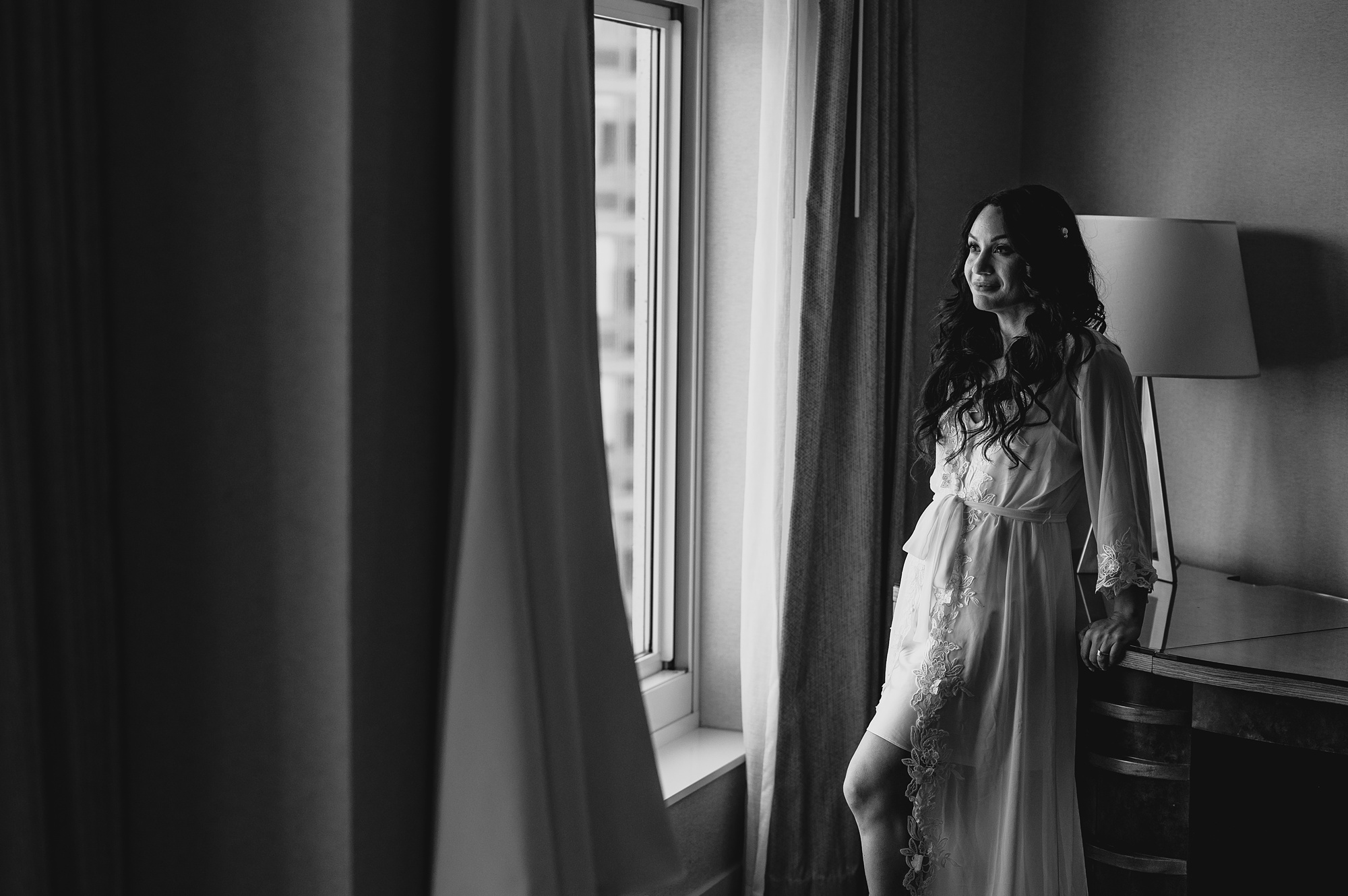 bride looks at wedding dress hanging in window of New Jersey hotel room