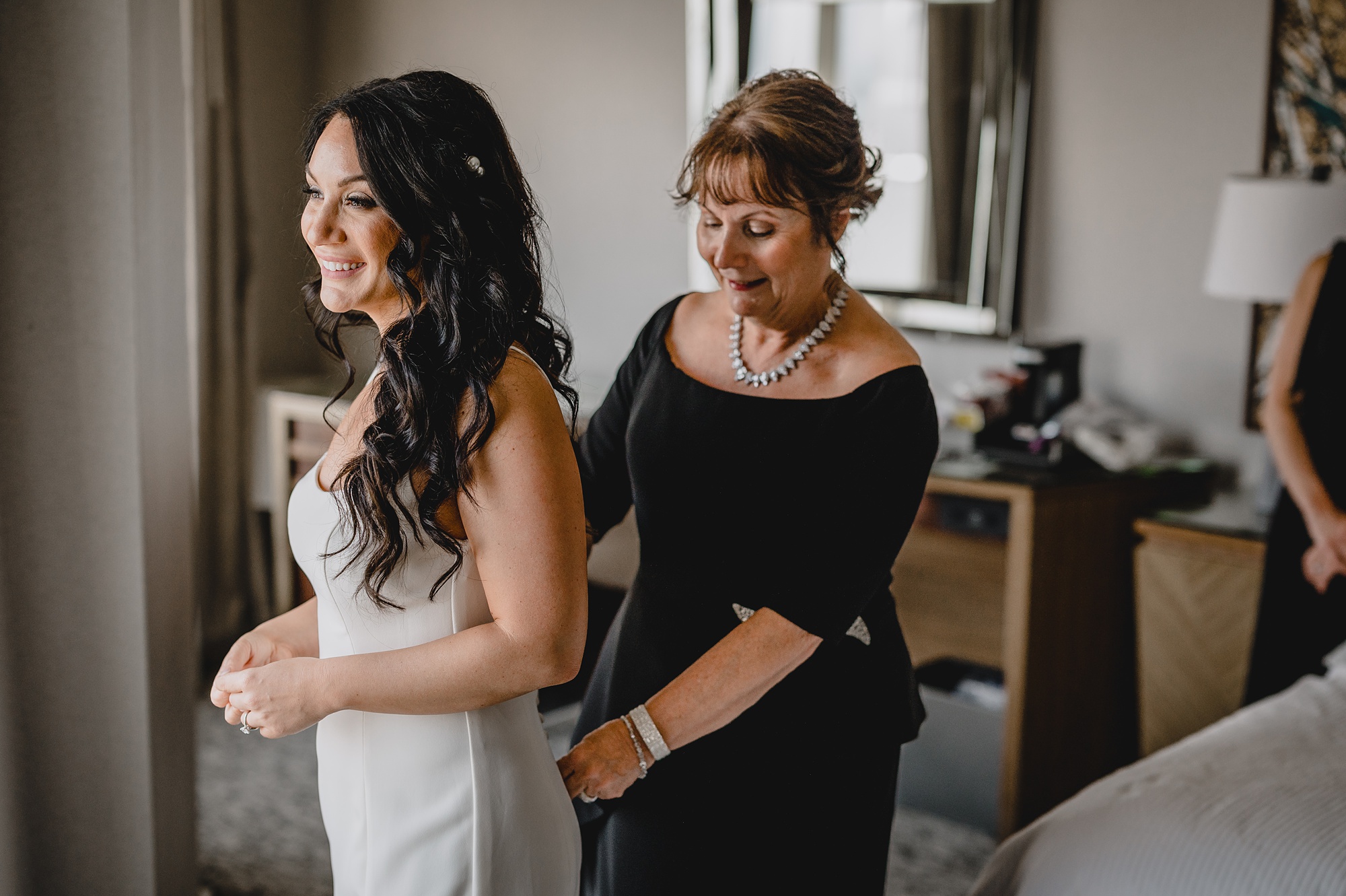 mother in black gown helps zip bride not wedding dress