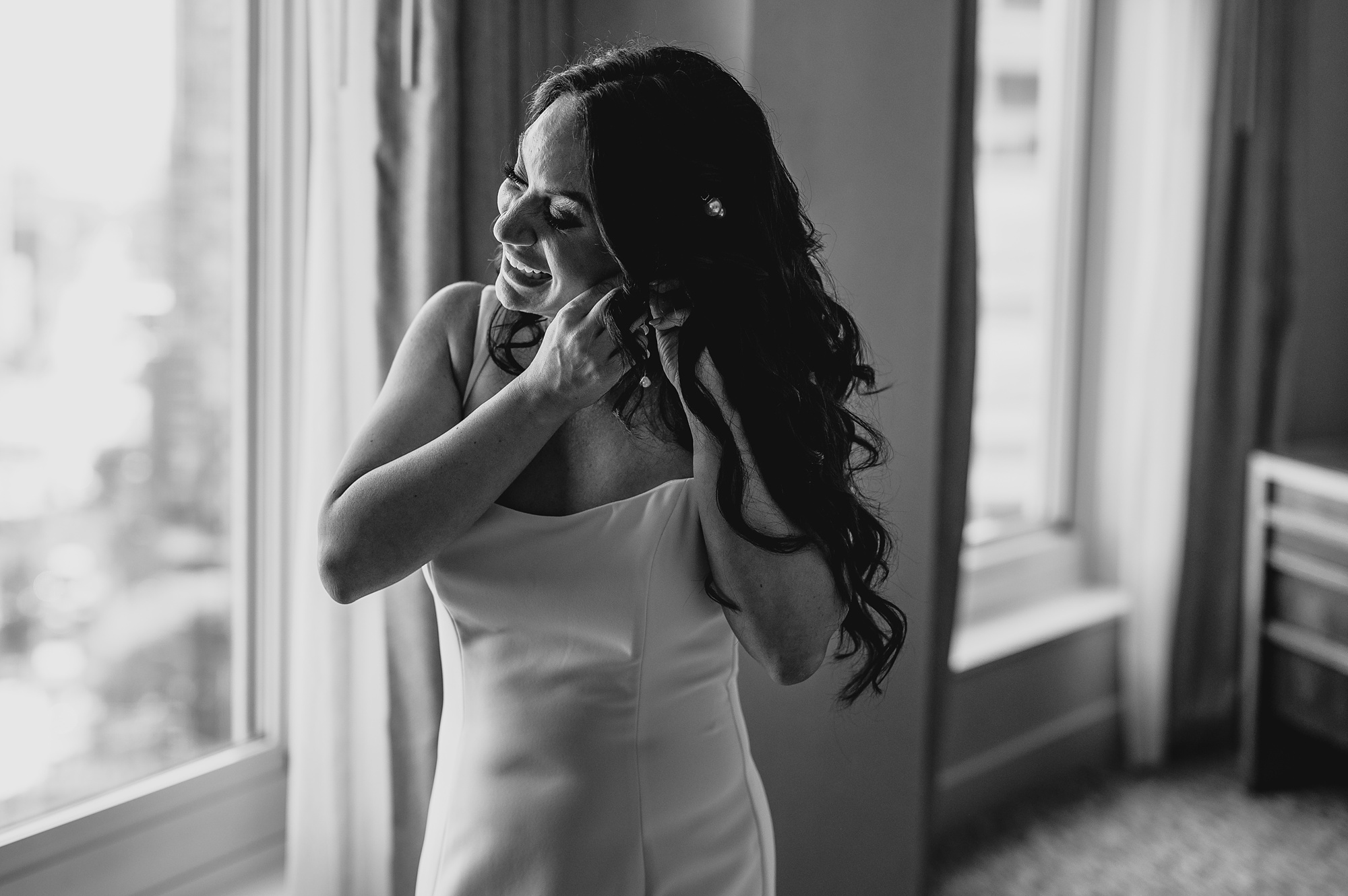 bride leans to adjust earring under hair in hotel room