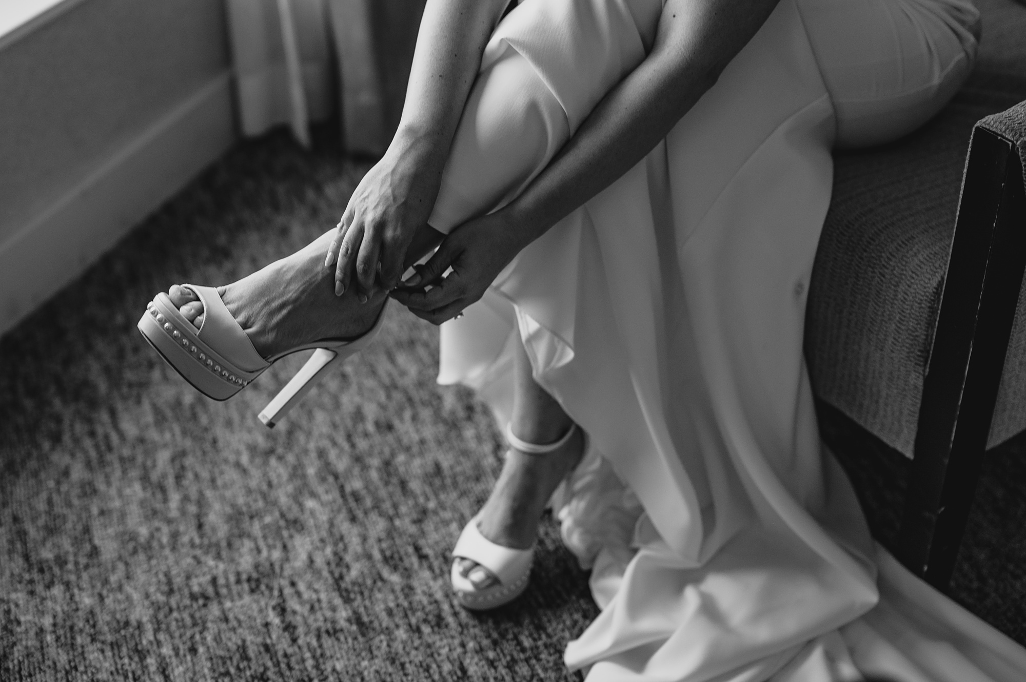 bride puts on white shoes in New Jersey hotel room