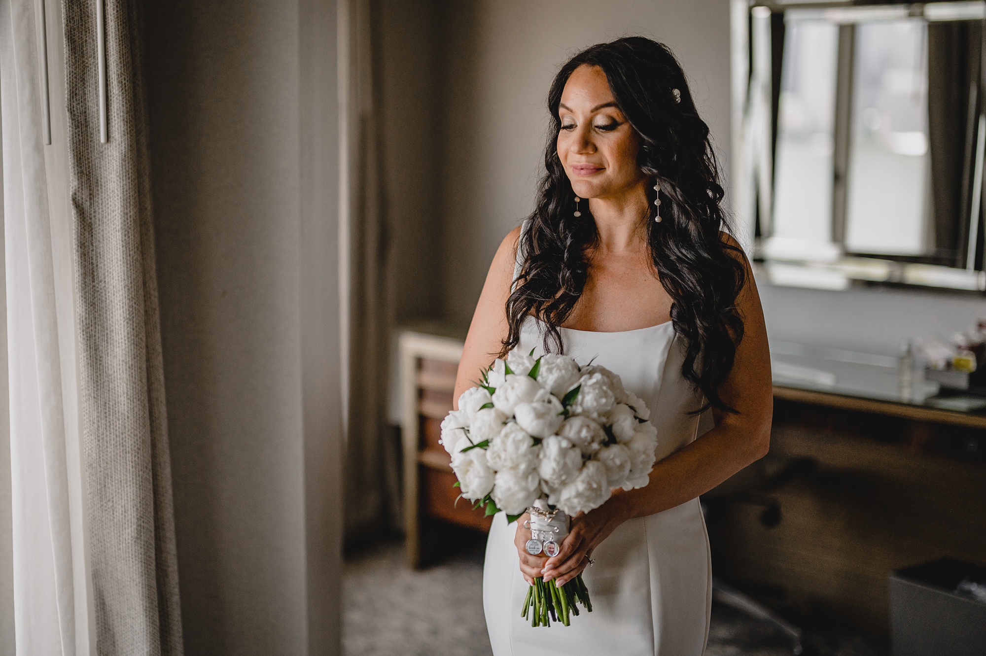 bride in strapless gown holds bouquet of ivory flowers in New Jersey hotel room