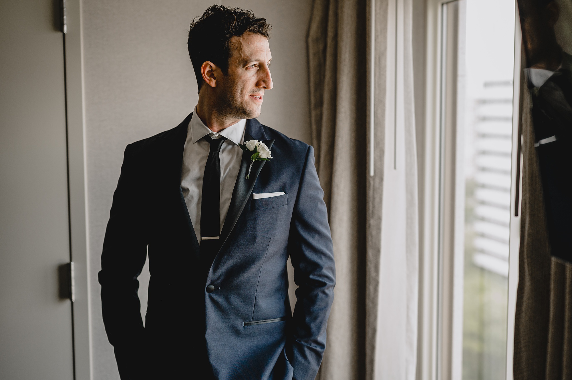 groom in navy suit jacket looks out window at New Jersey hotel