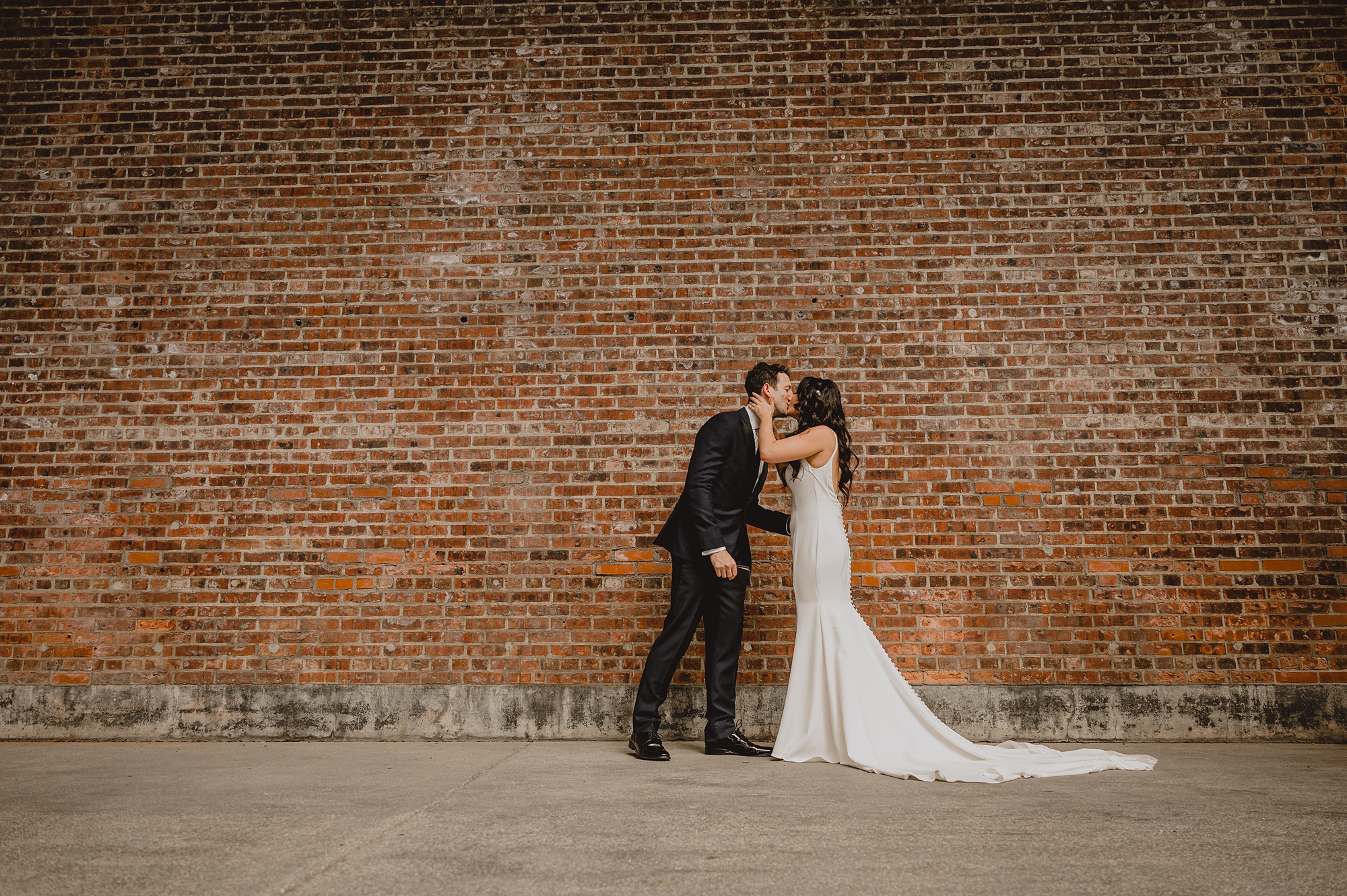 newlyweds kiss in front of brick wall at the Liberty House