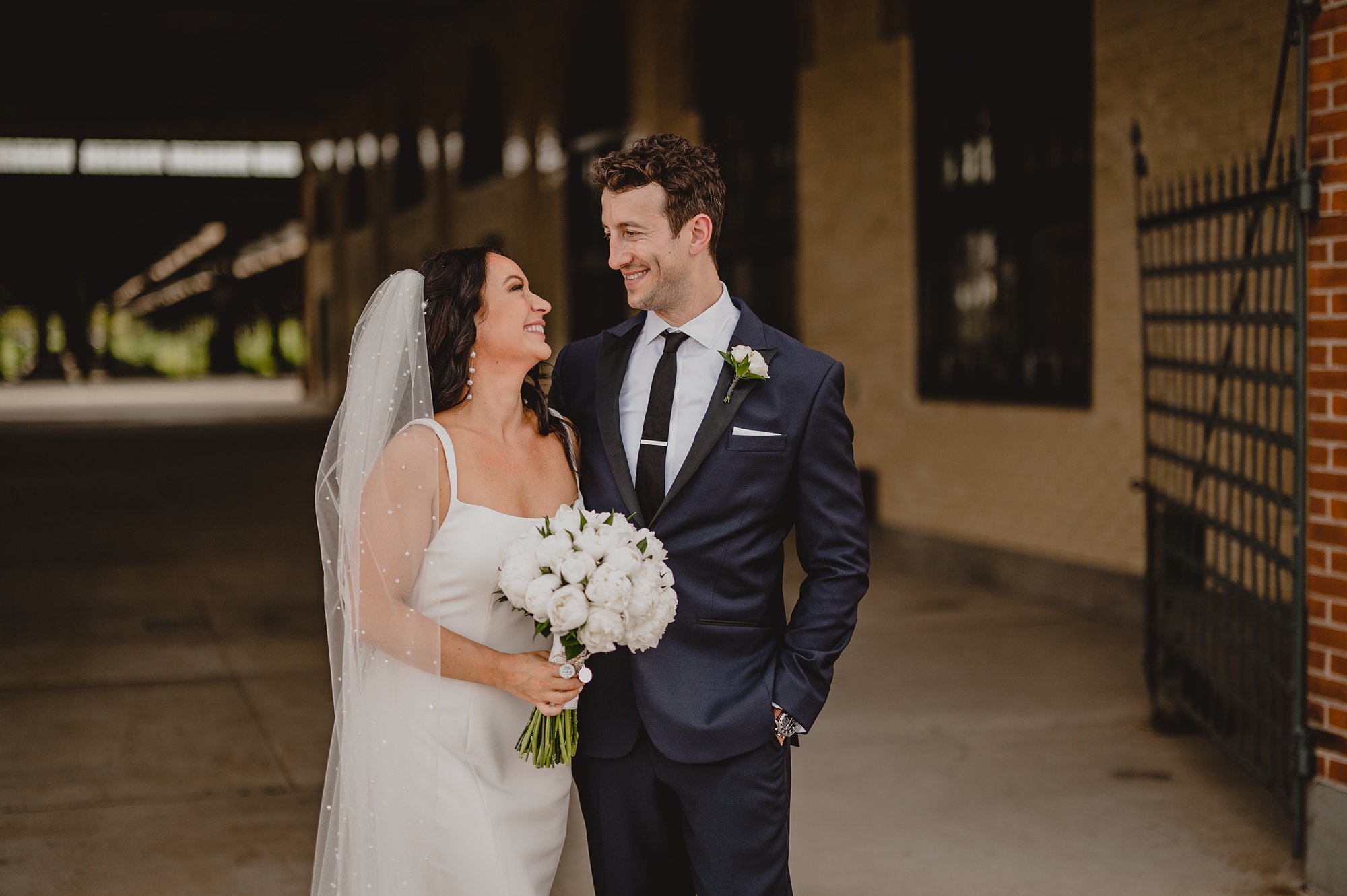 groom in grey suit smiles at bride hugging her to him