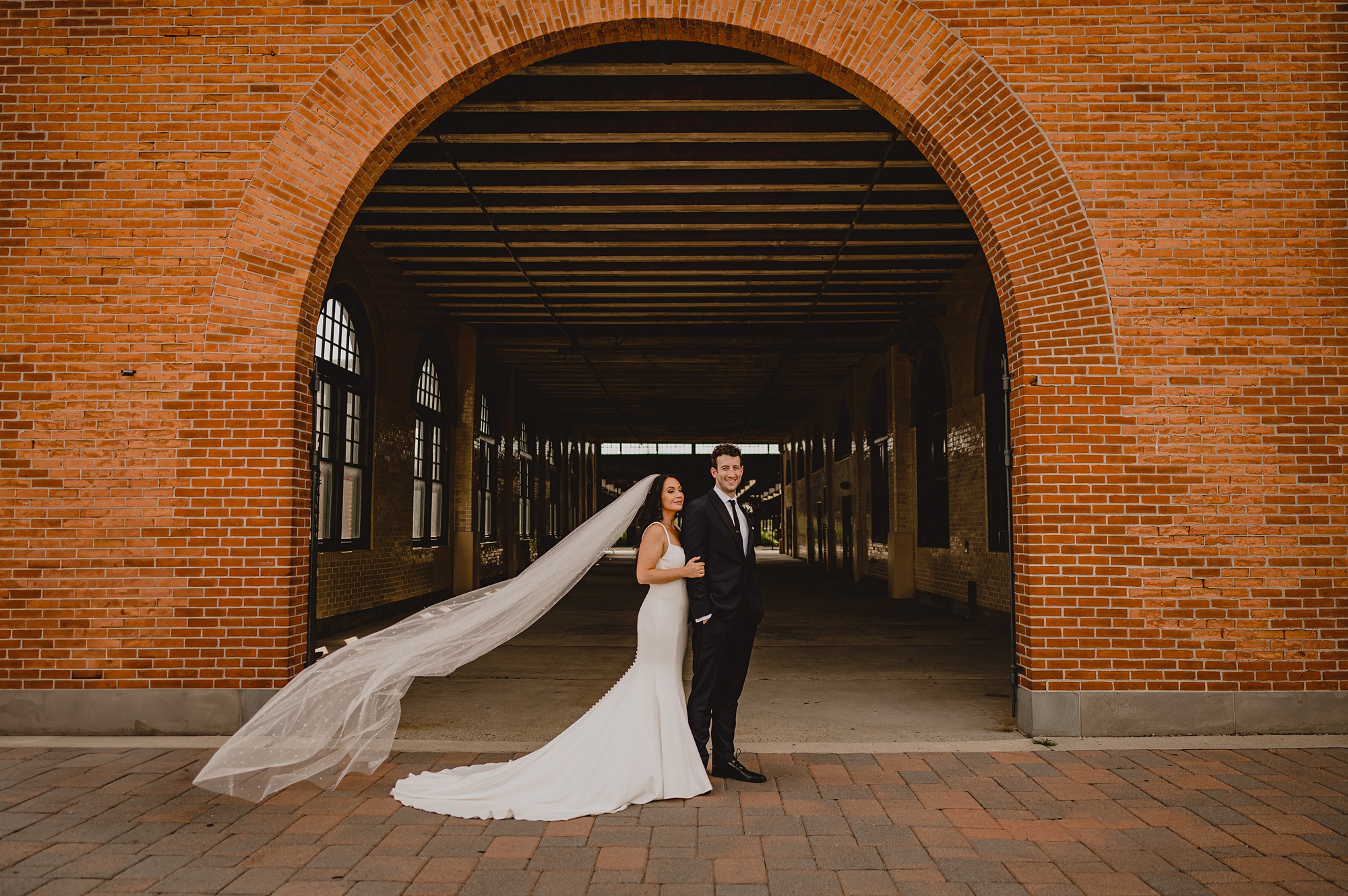 bride hugs groom from behind with veil floating outside the Liberty House