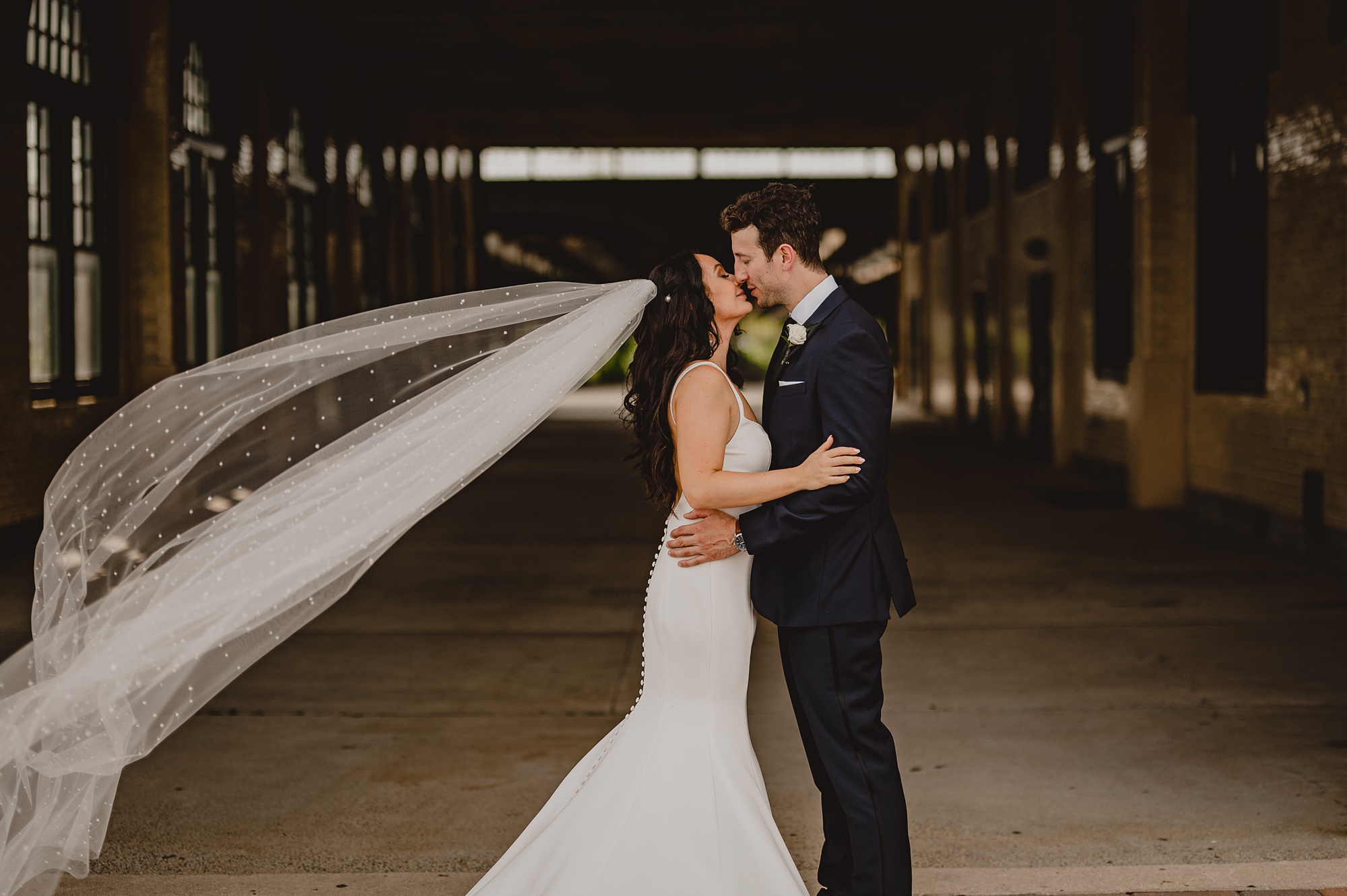 bride and groom kiss with bride's veil floating behind them