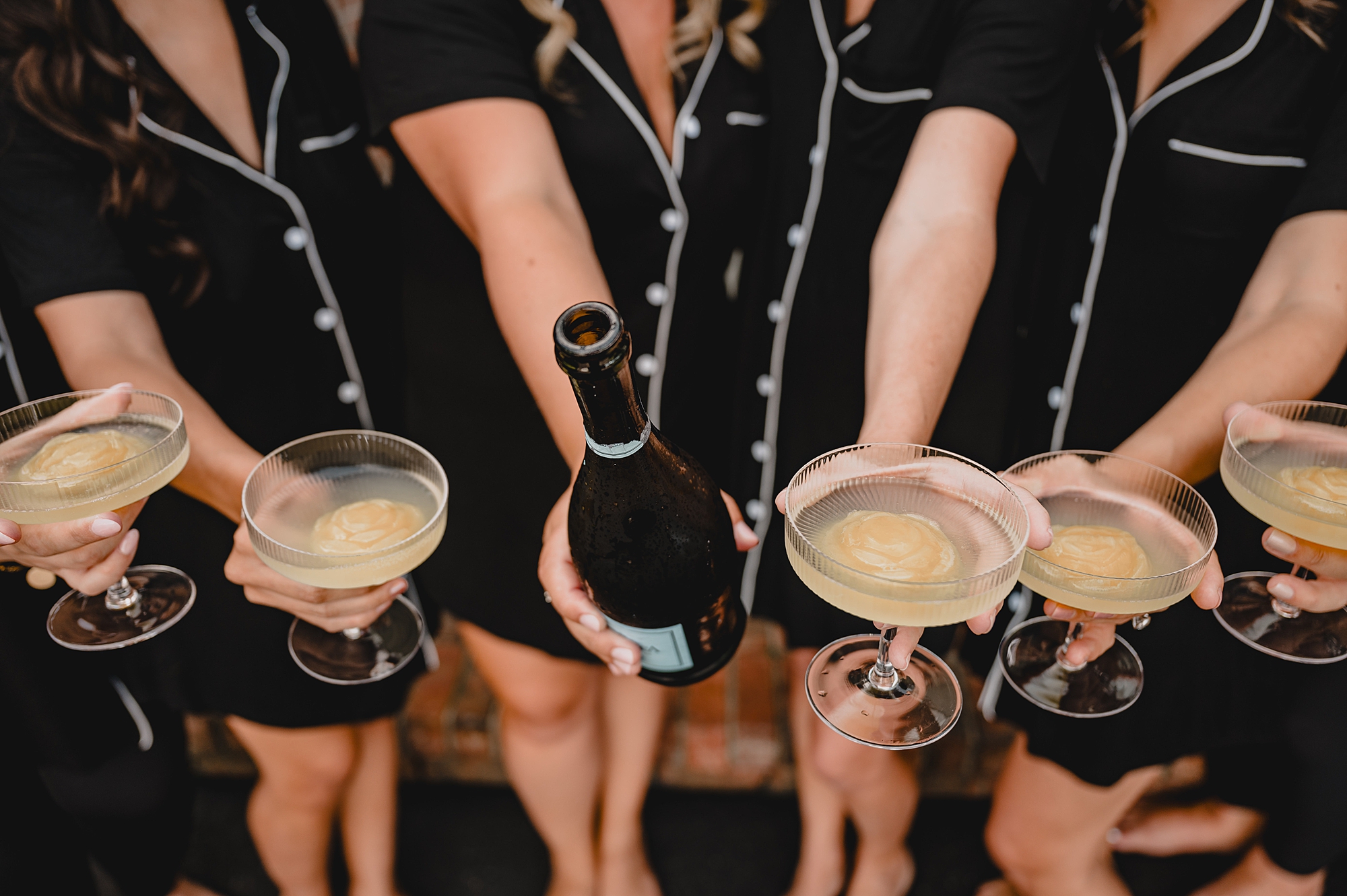 bride holds bottle of champagne with bridesmaids around her