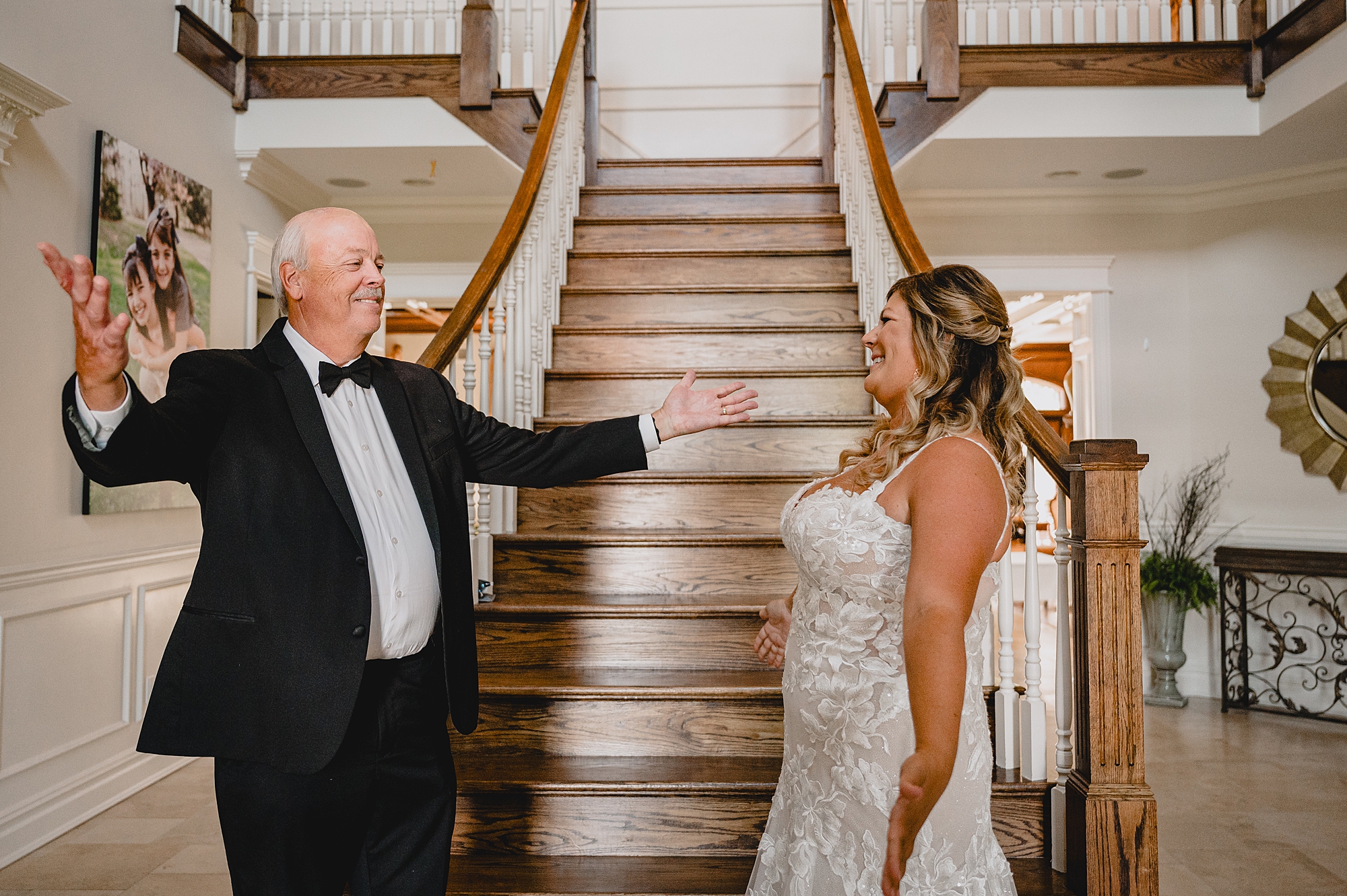 father goes to hug bride during first look at base of staircase inside the Mill Lakeside Manor