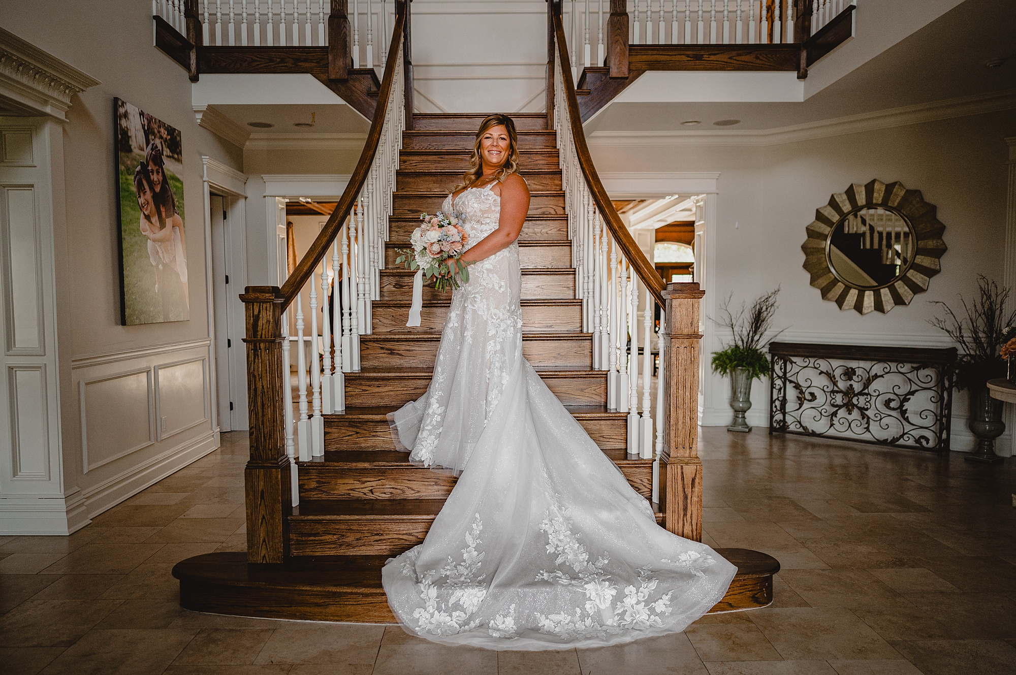 bride stands holding bouquet of flowers on staircase inside the Mill Lakeside Manor
