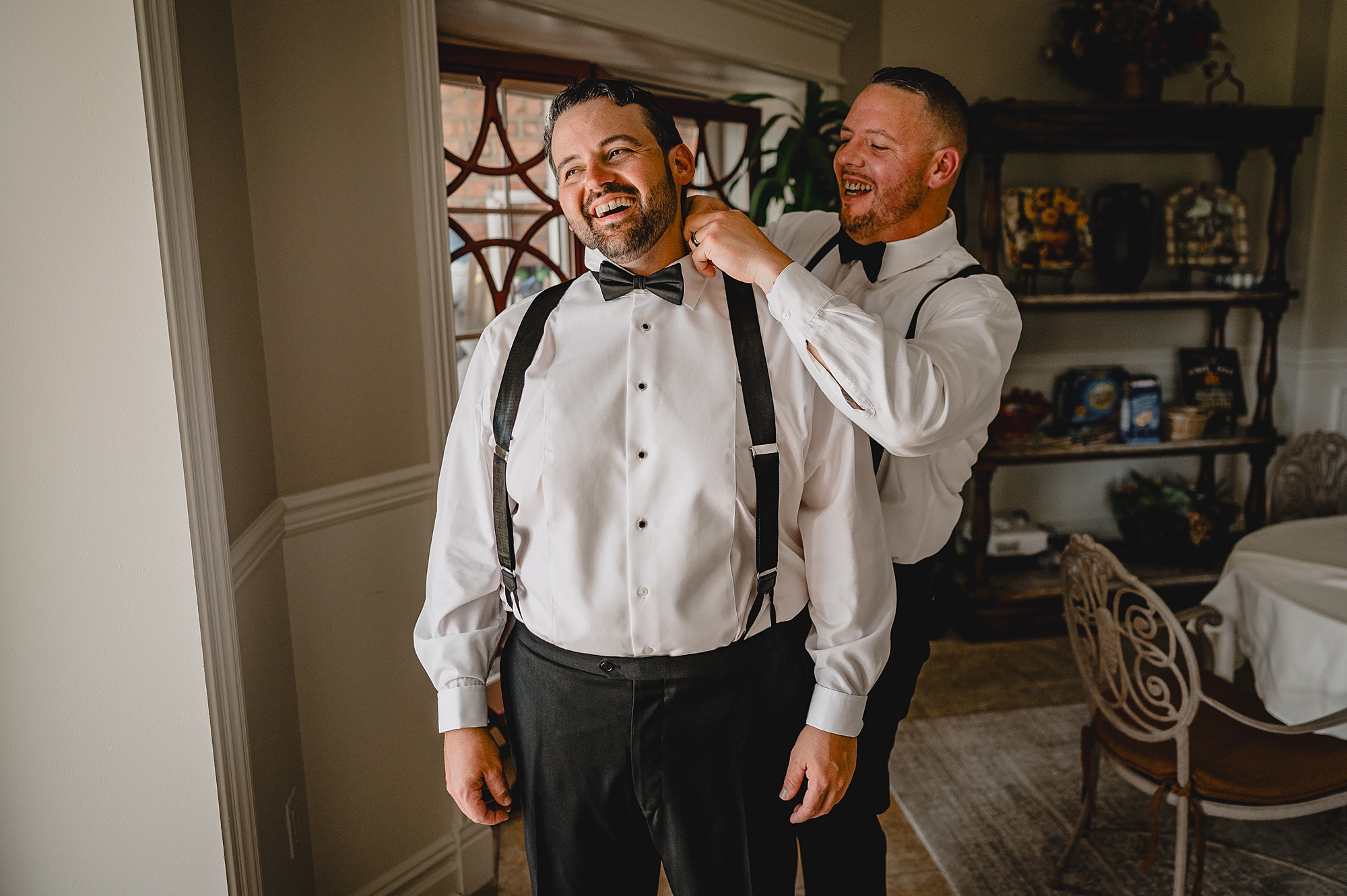groomsman helps groom with bowtie for suit at the Mill Lakeside Manor