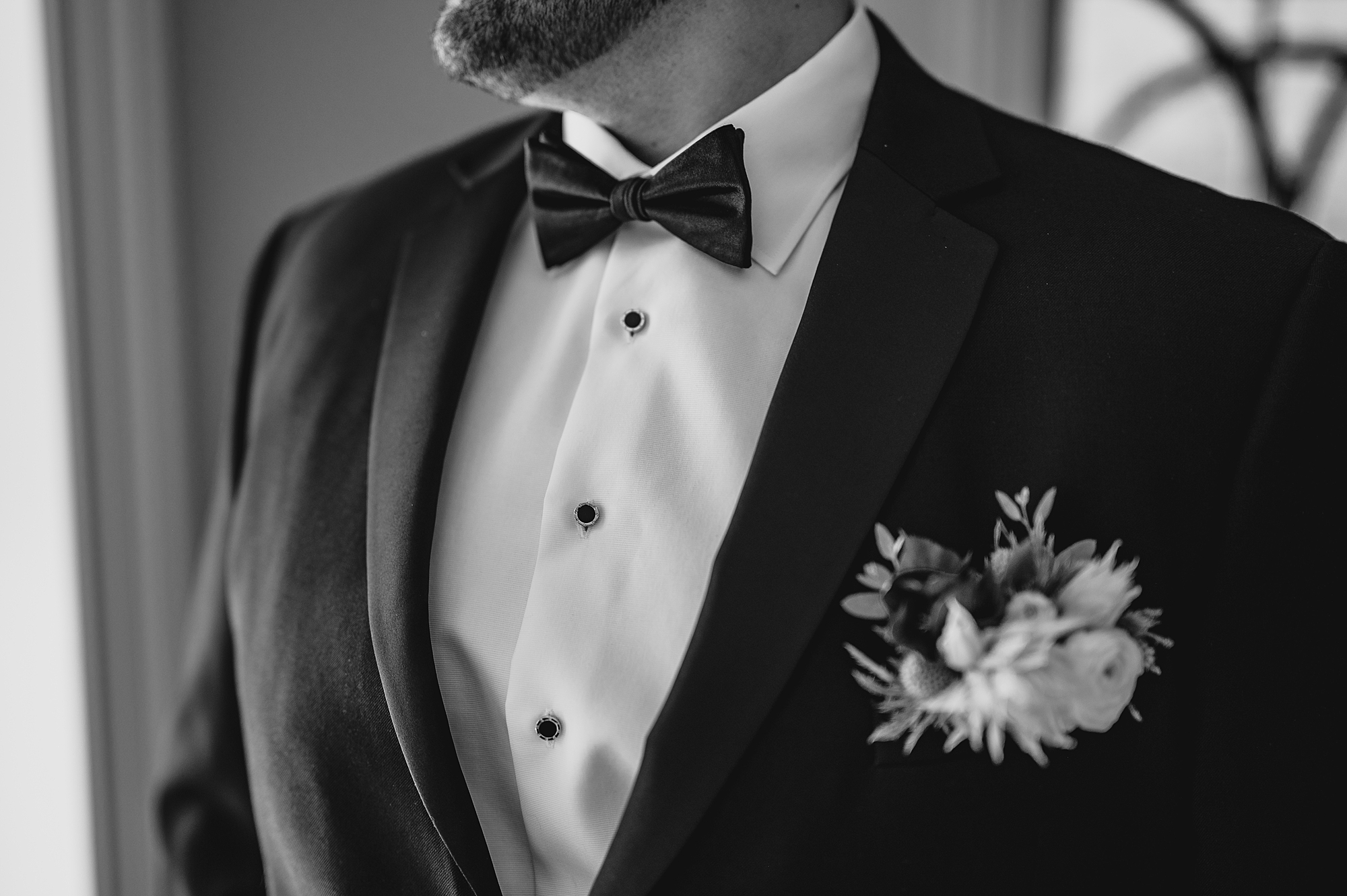 groom stands in black suit with wildflower boutonnière for fall wedding at the Mill Lakeside Manor