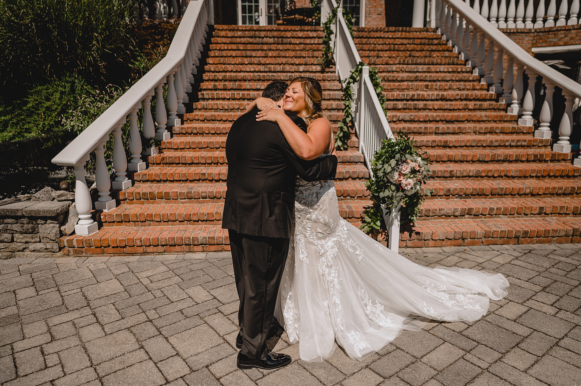 newlyweds hug by brick staircase during first look at the Mill Lakeside Manor