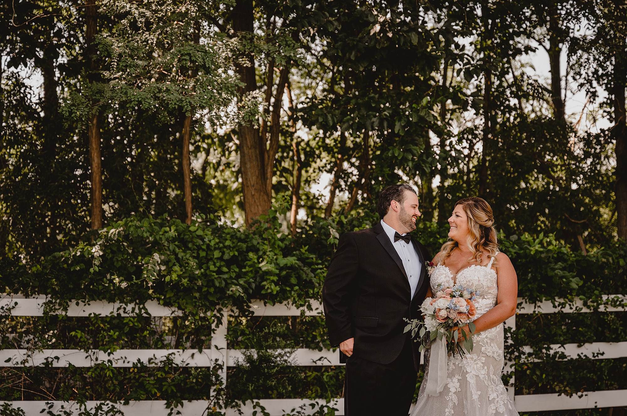 bride smiles up at groom standing by white wooden fence in New Jersey