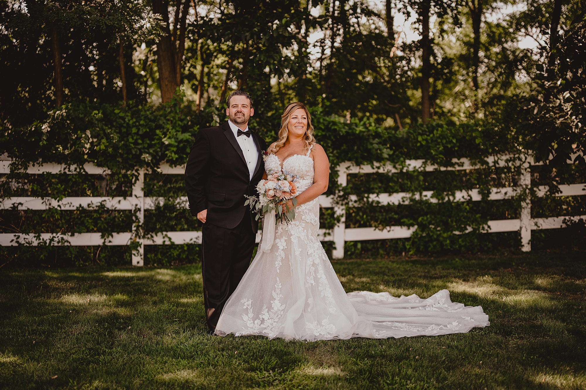 newlyweds stand by white fence in yard at the Mill Lakeside Manor